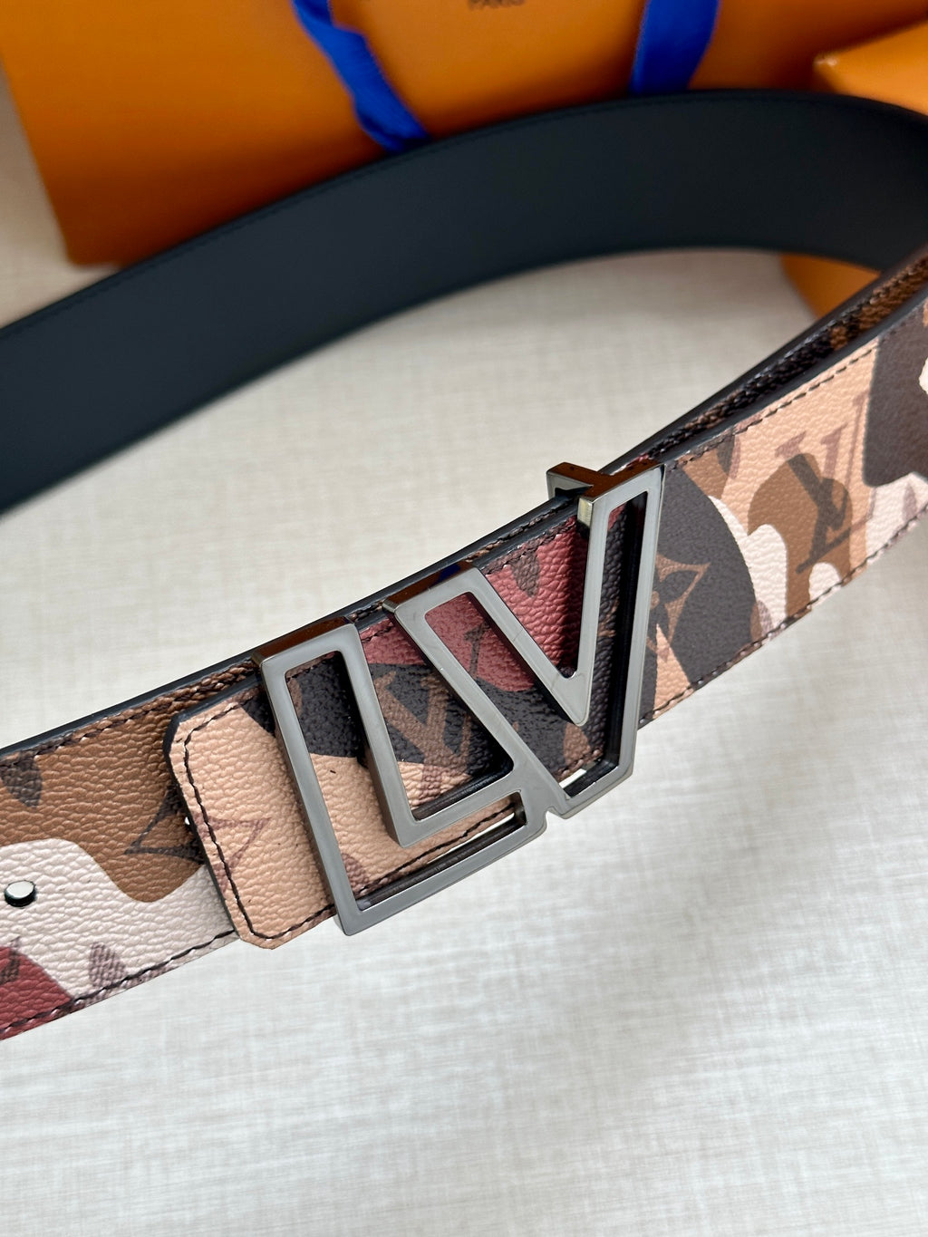 Designer belt close-up featuring gold-tone LV buckle on patterned leather strap