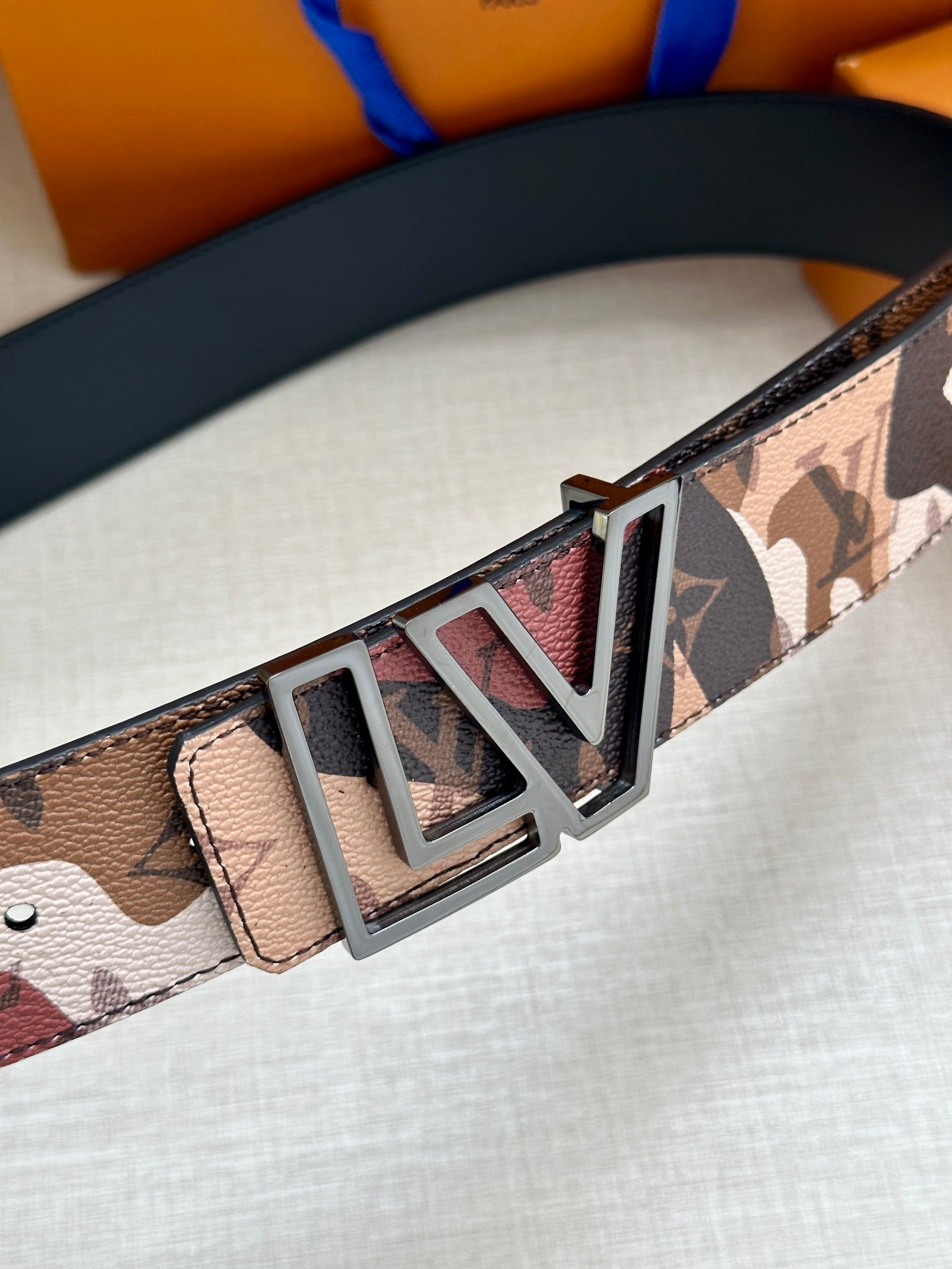 Designer belt close-up featuring gold-tone LV buckle on patterned leather strap