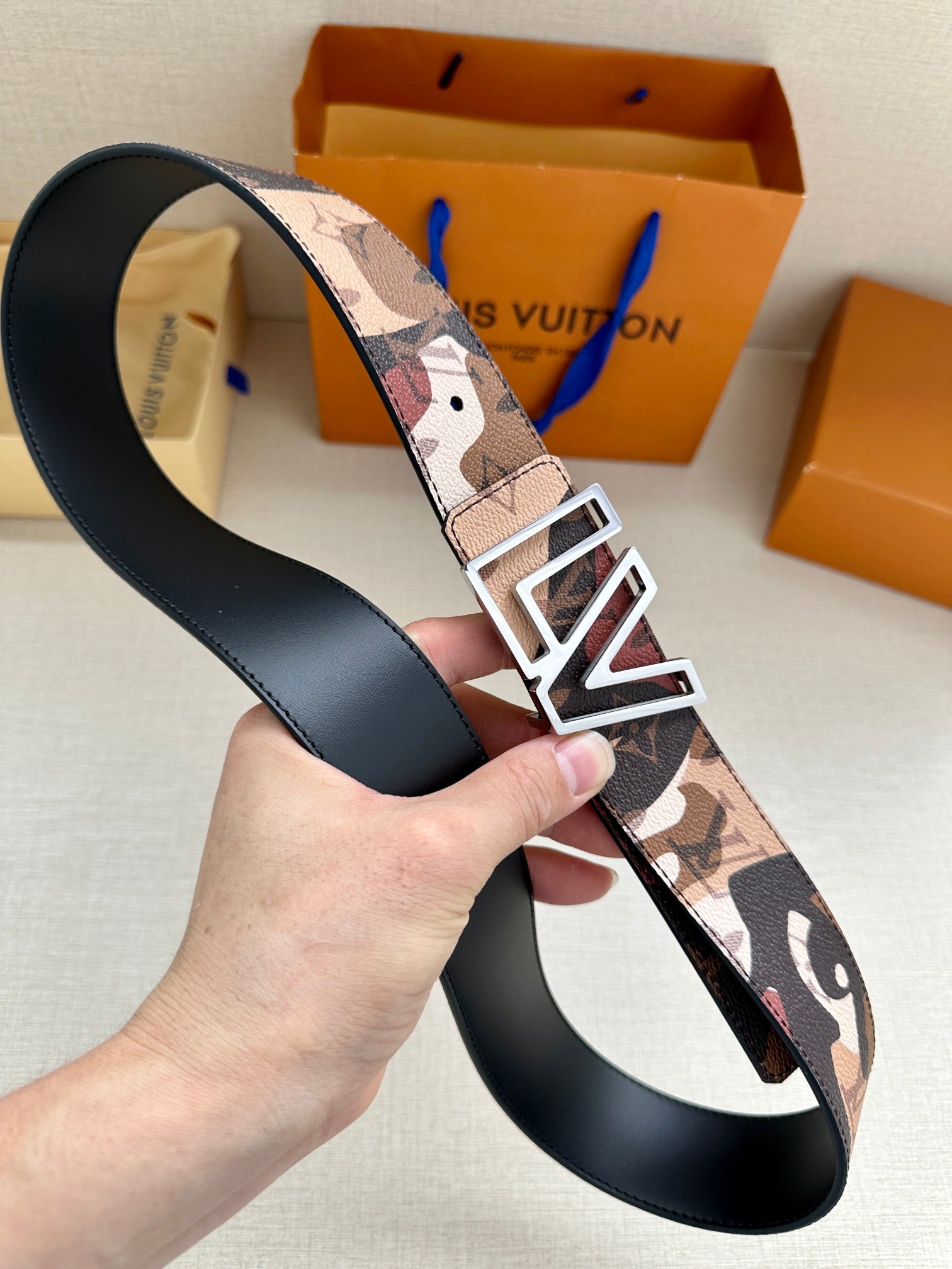 Designer belt shown at an angle, patterned strap with gold-tone LV buckle