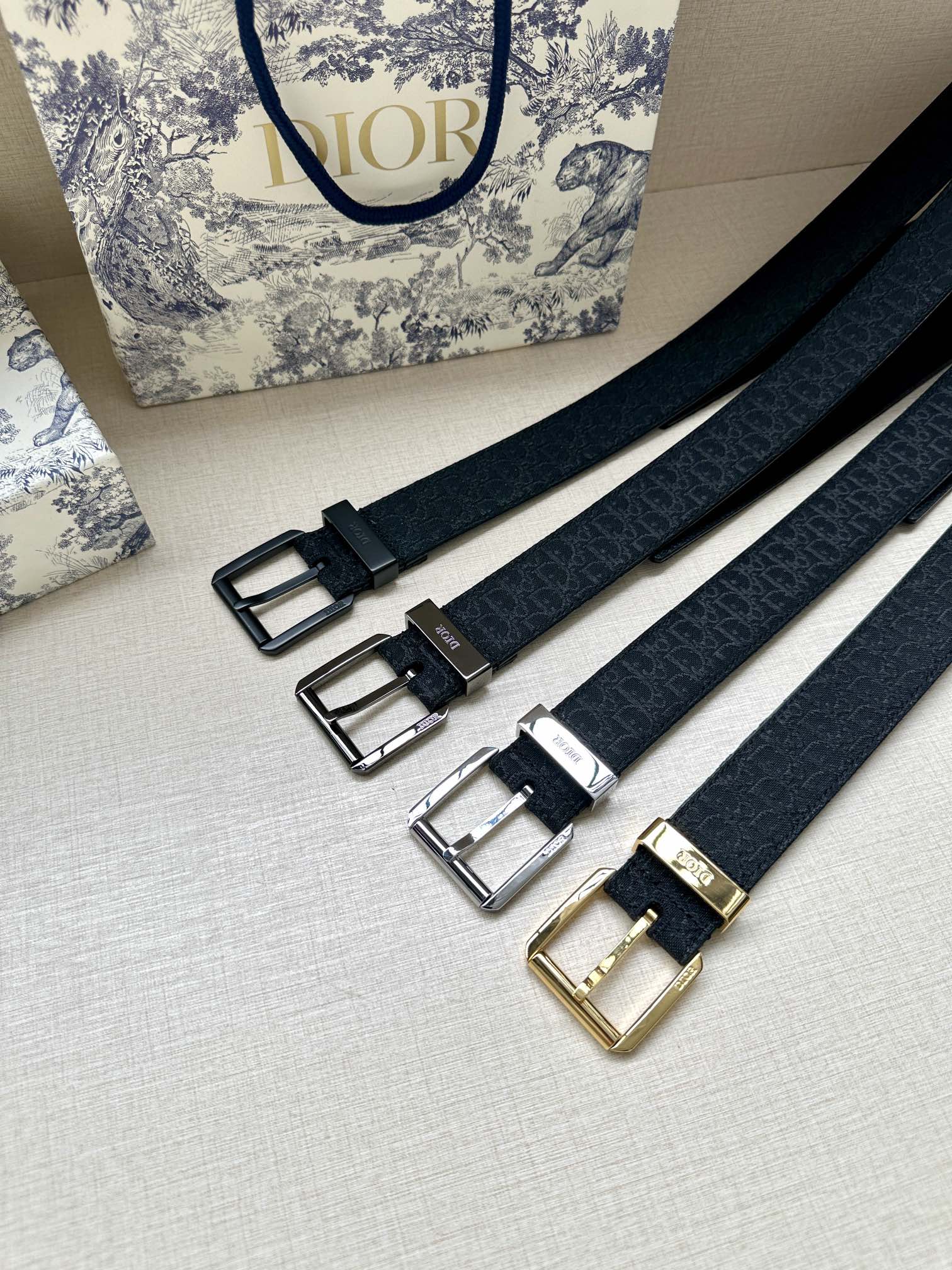 Multiple Dior belt straps with different buckle finishes: black, silver, and gold