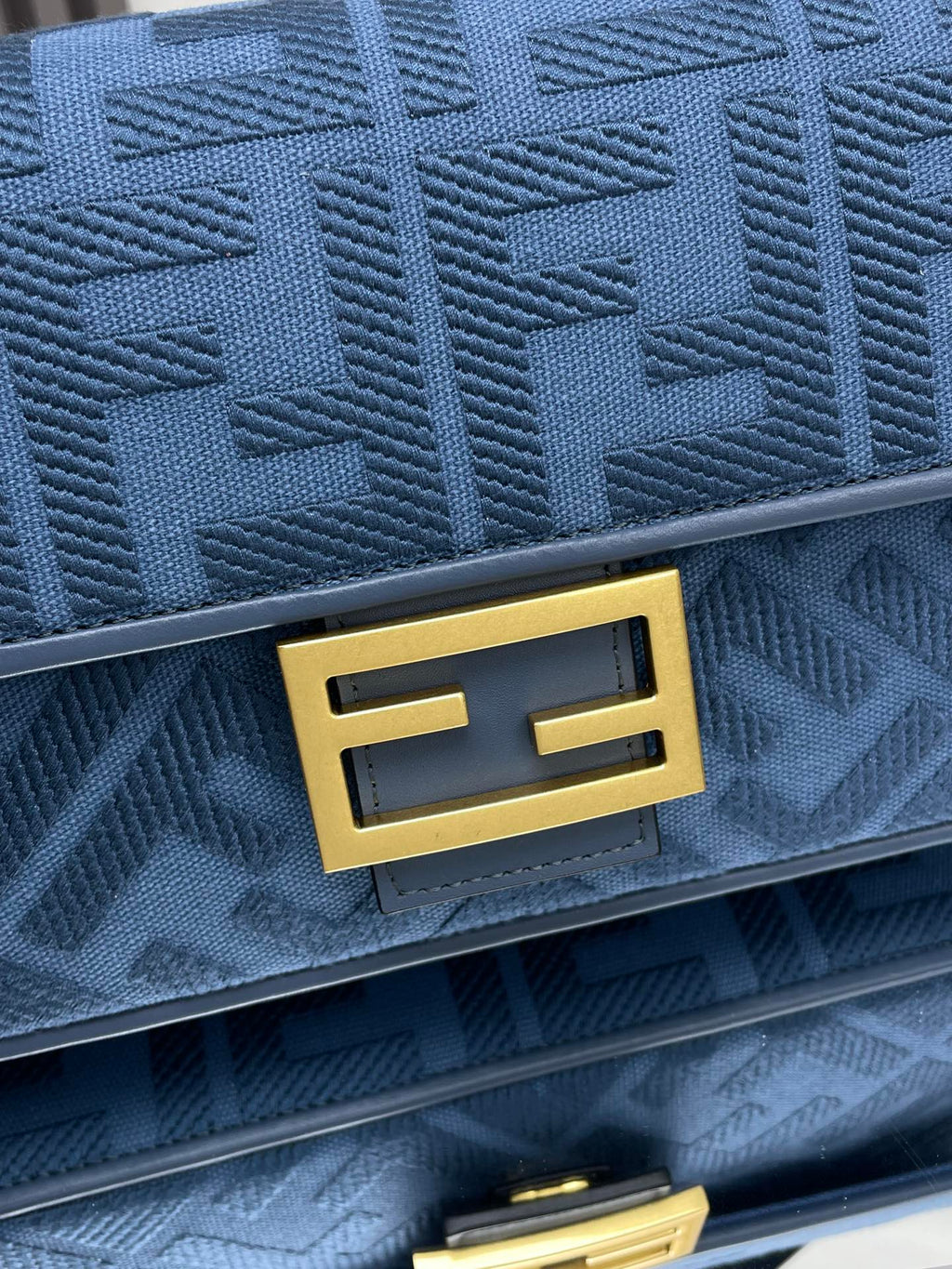 Blue Fendi bag close-up: gold B-shaped logo plaque on textured fabric flap
