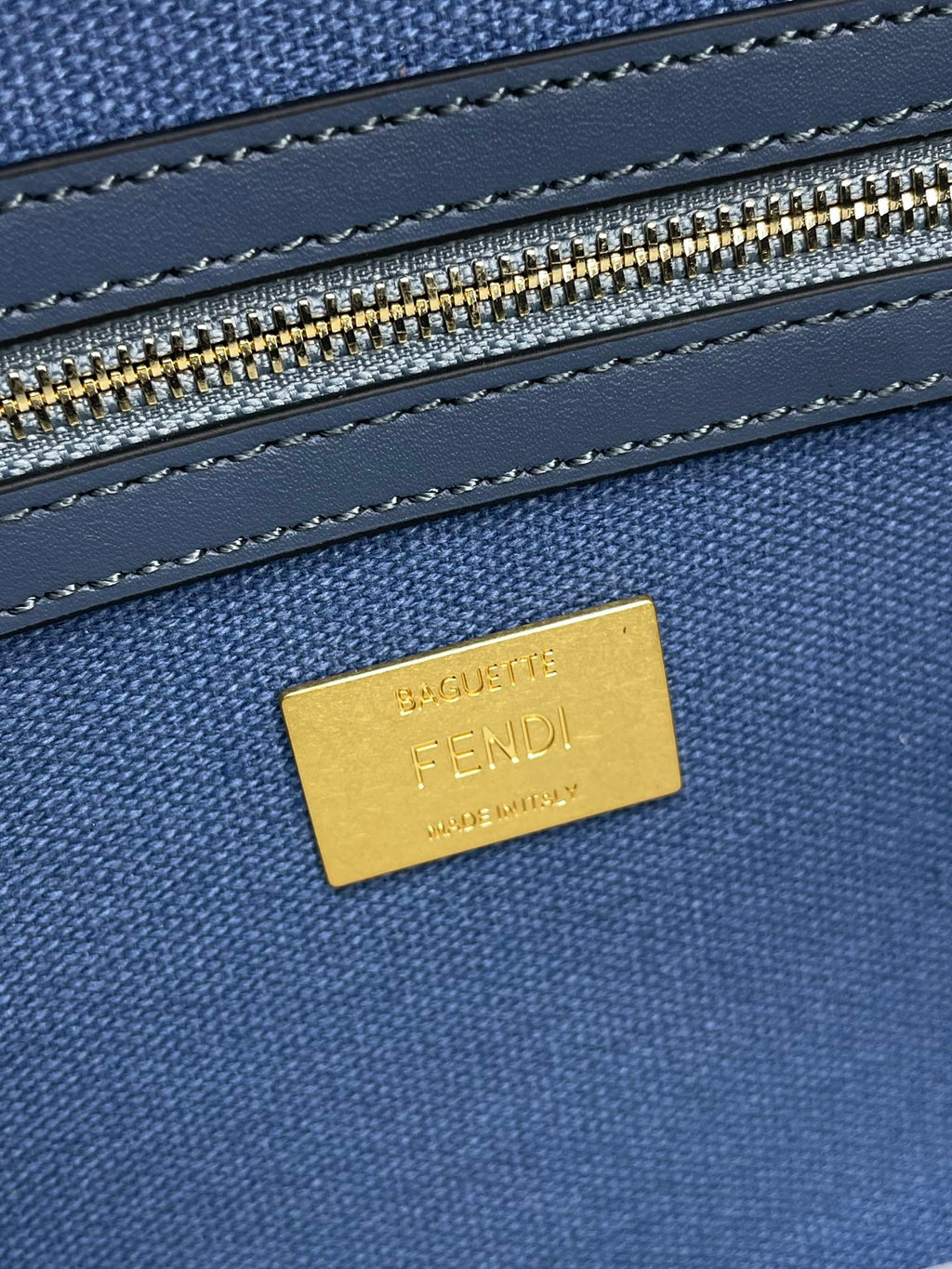 Gold Fendi label on blue textured bag with stitched trim and zipper track