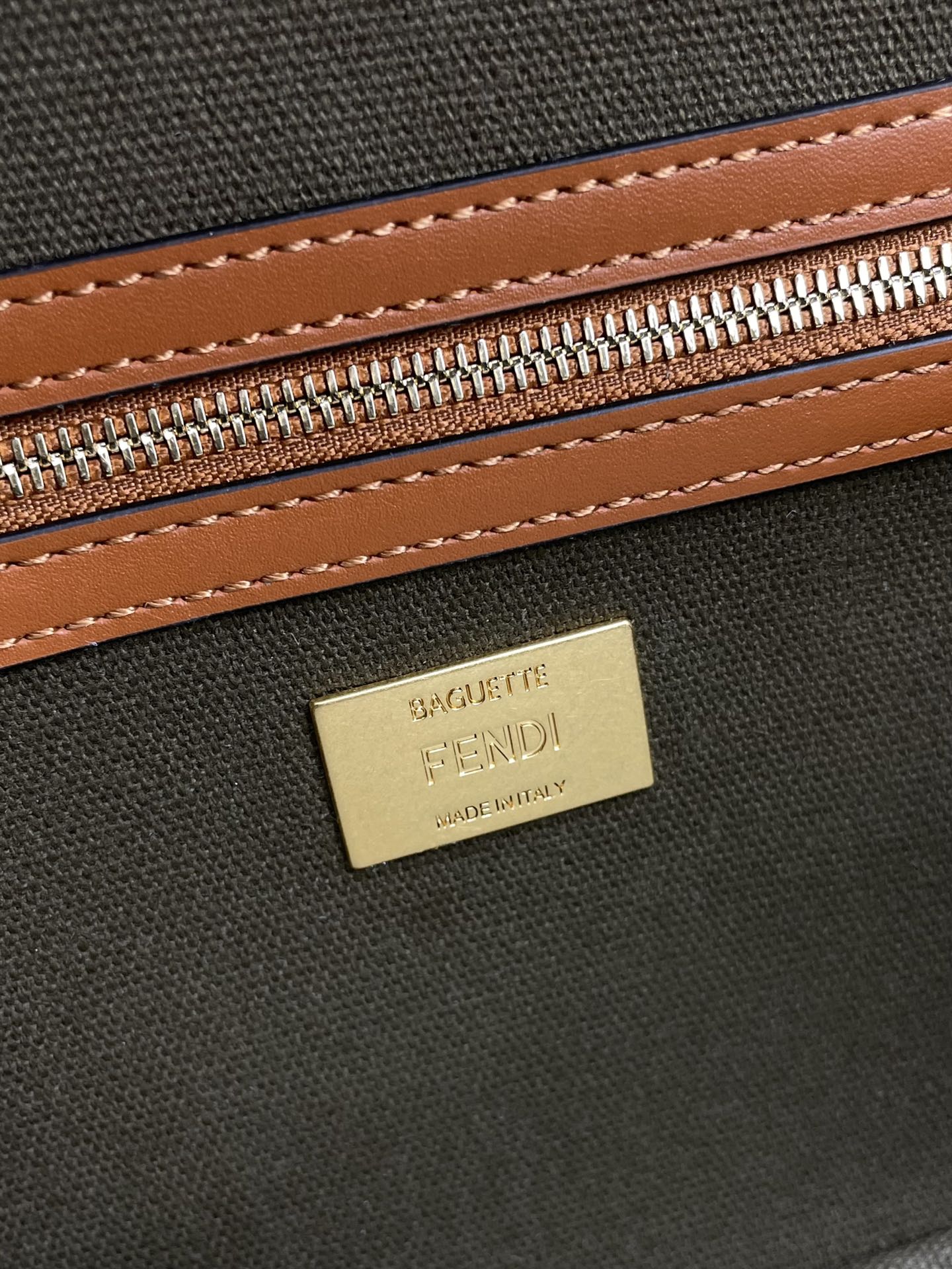 Fendi zip pouch close-up with gold logo plate and brown-stitched trim