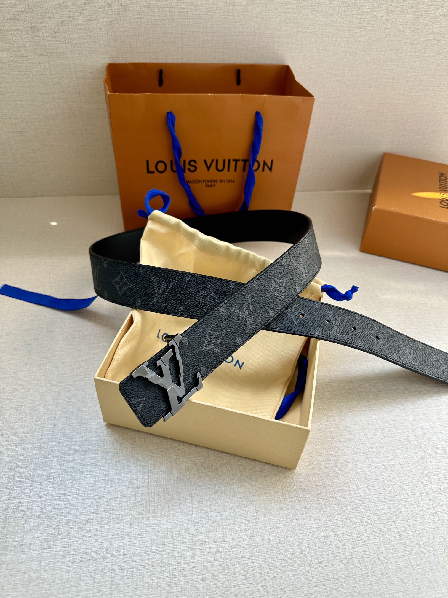 Dark monogram leather belt with wide strap and metal buckle, laid over box