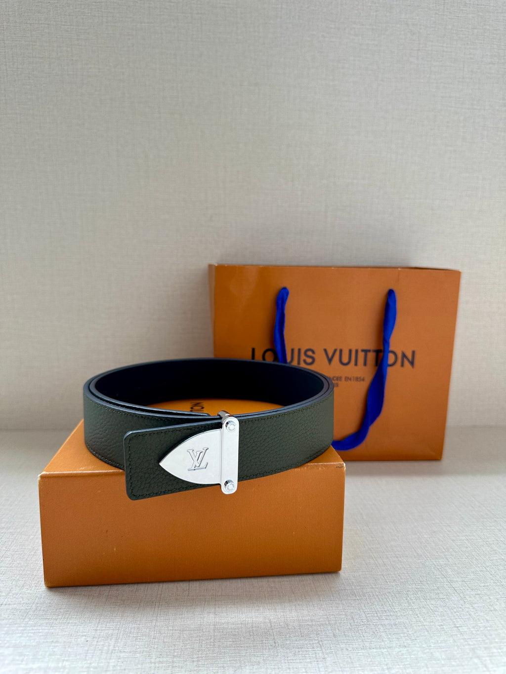 Louis Vuitton leather belt dark green with silver buckle, laid across orange box