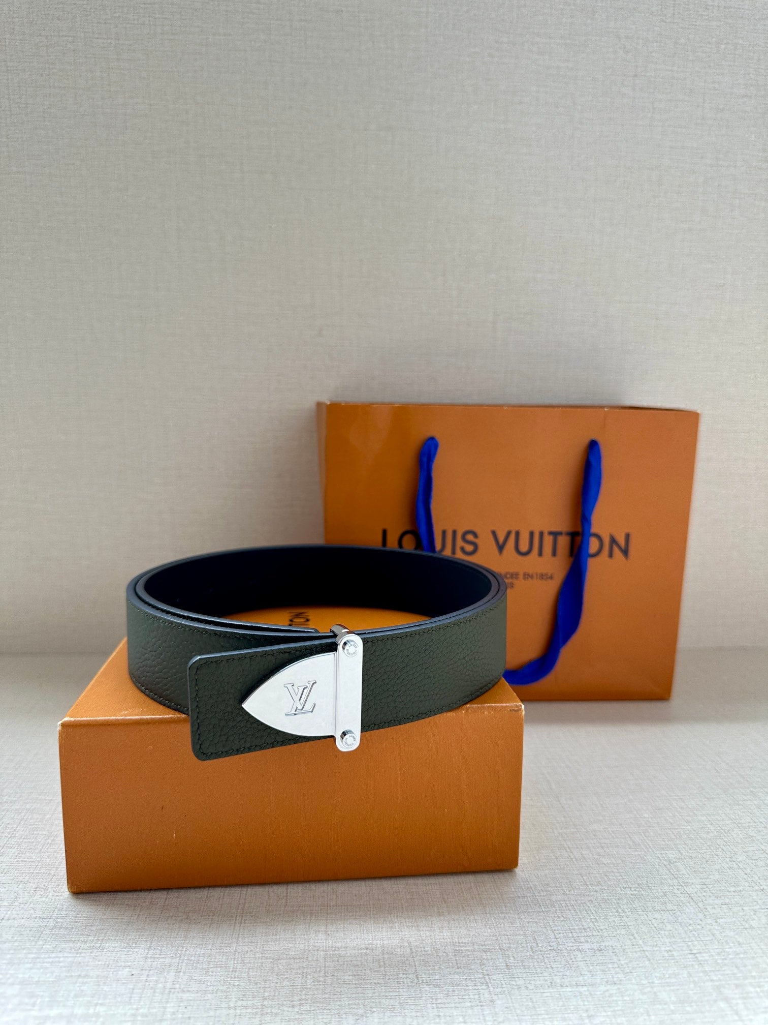 Louis Vuitton leather belt dark green with silver buckle, laid across orange box