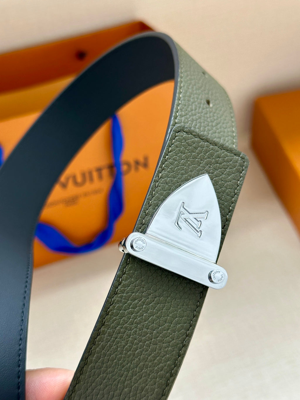 Louis Vuitton leather belt close-up: dark green strap with silver-tone logo buckle