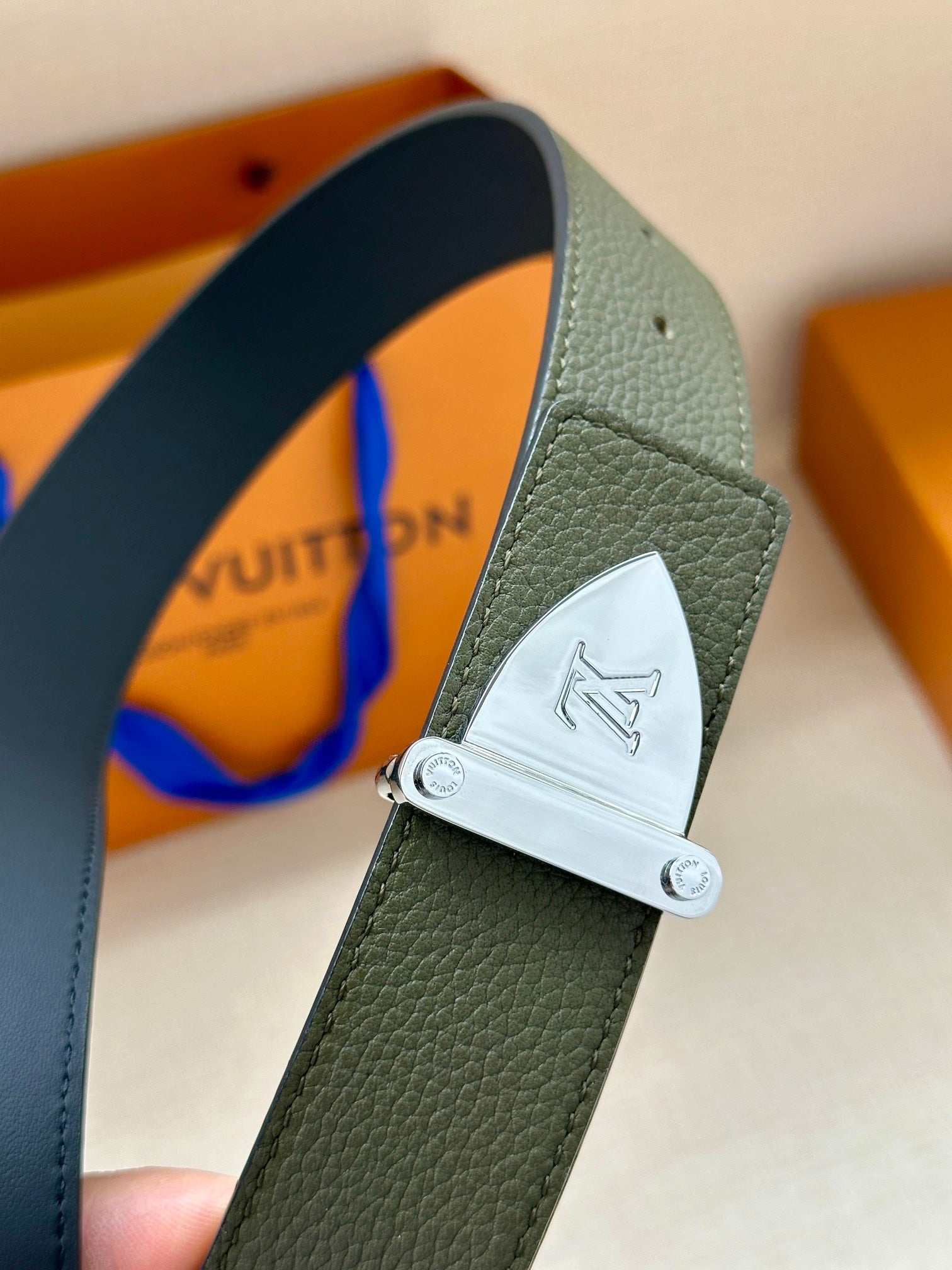 Louis Vuitton leather belt close-up: dark green strap with silver-tone logo buckle
