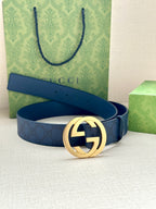 Gucci belt with navy textured strap and round gold-tone GG buckle, laid flat