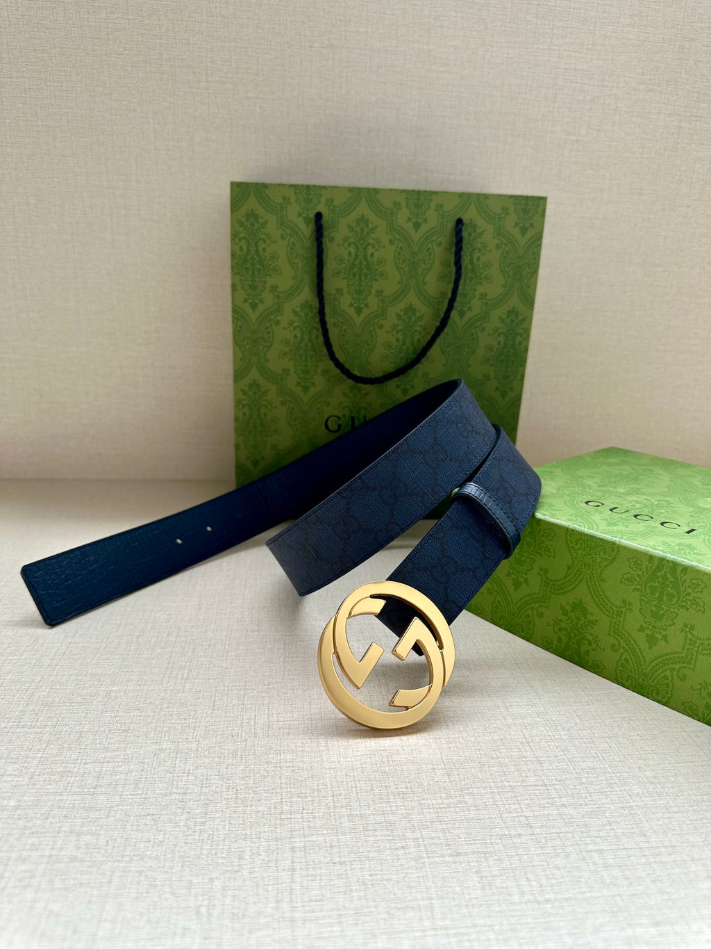 Gucci belt with navy strap and gold-tone GG buckle, resting on folded packaging