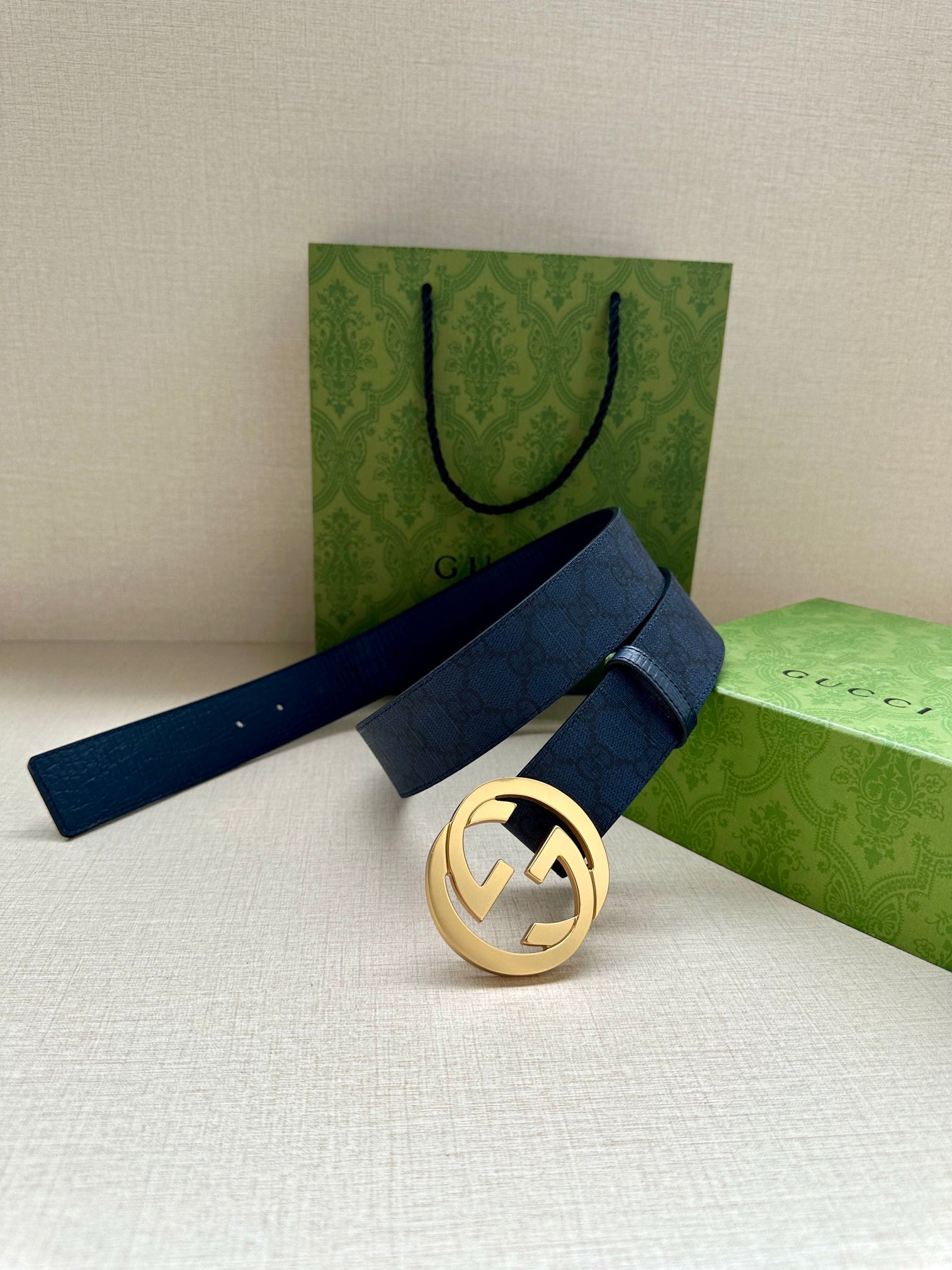 Gucci belt with navy strap and gold-tone GG buckle, resting on folded packaging