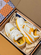 White and yellow low-top trainer sneakers in open box with lace-up uppers and logos