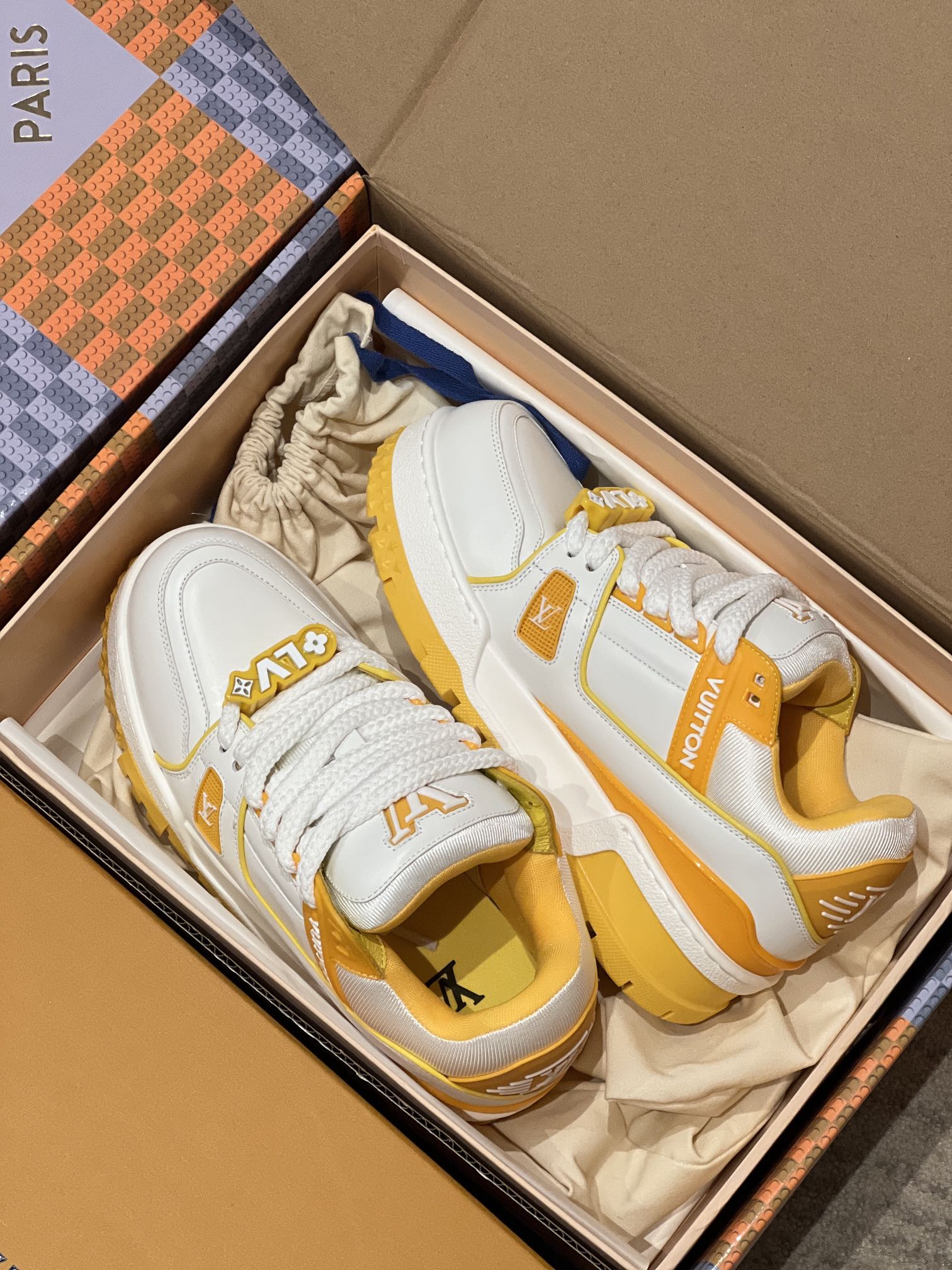 White and yellow low-top trainer sneakers in open box with lace-up uppers and logos
