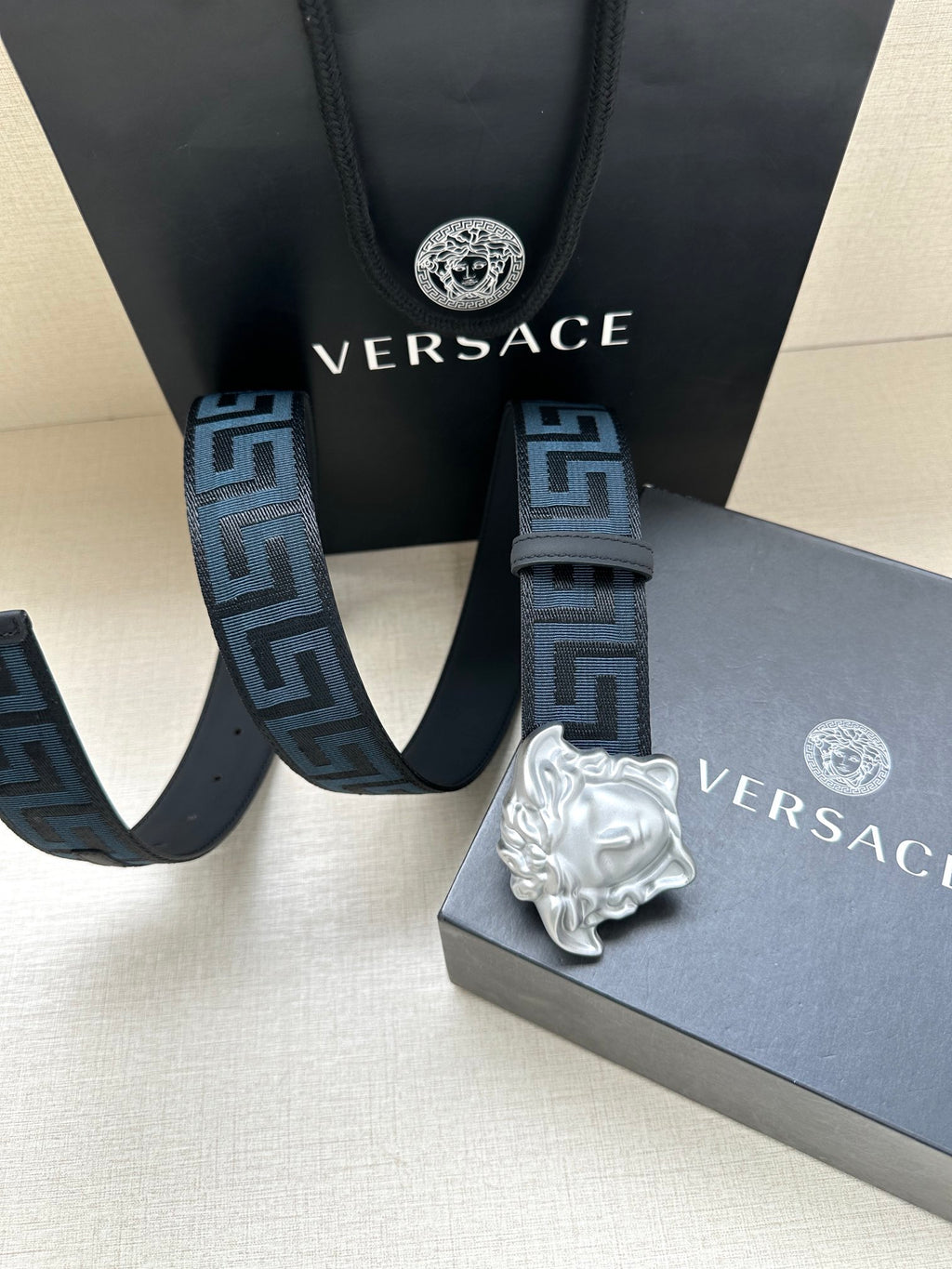 Versace belt close-up: dark blue Greek key straps with silver Medusa buckle.