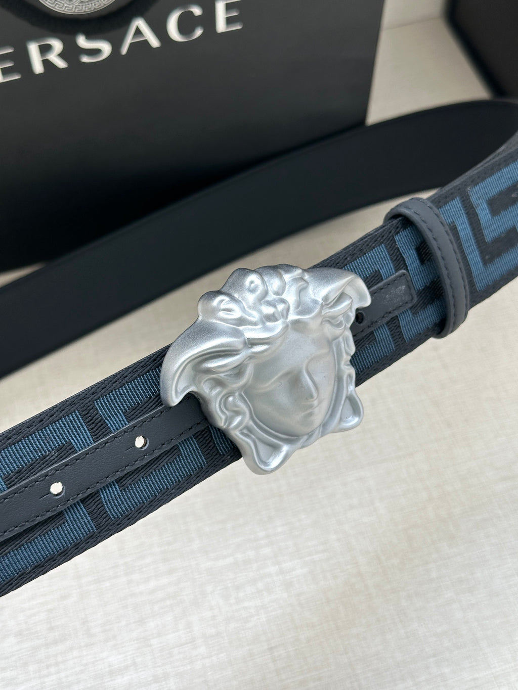 Versace belt detail: dark blue Greek key strap with silver Medusa buckle.