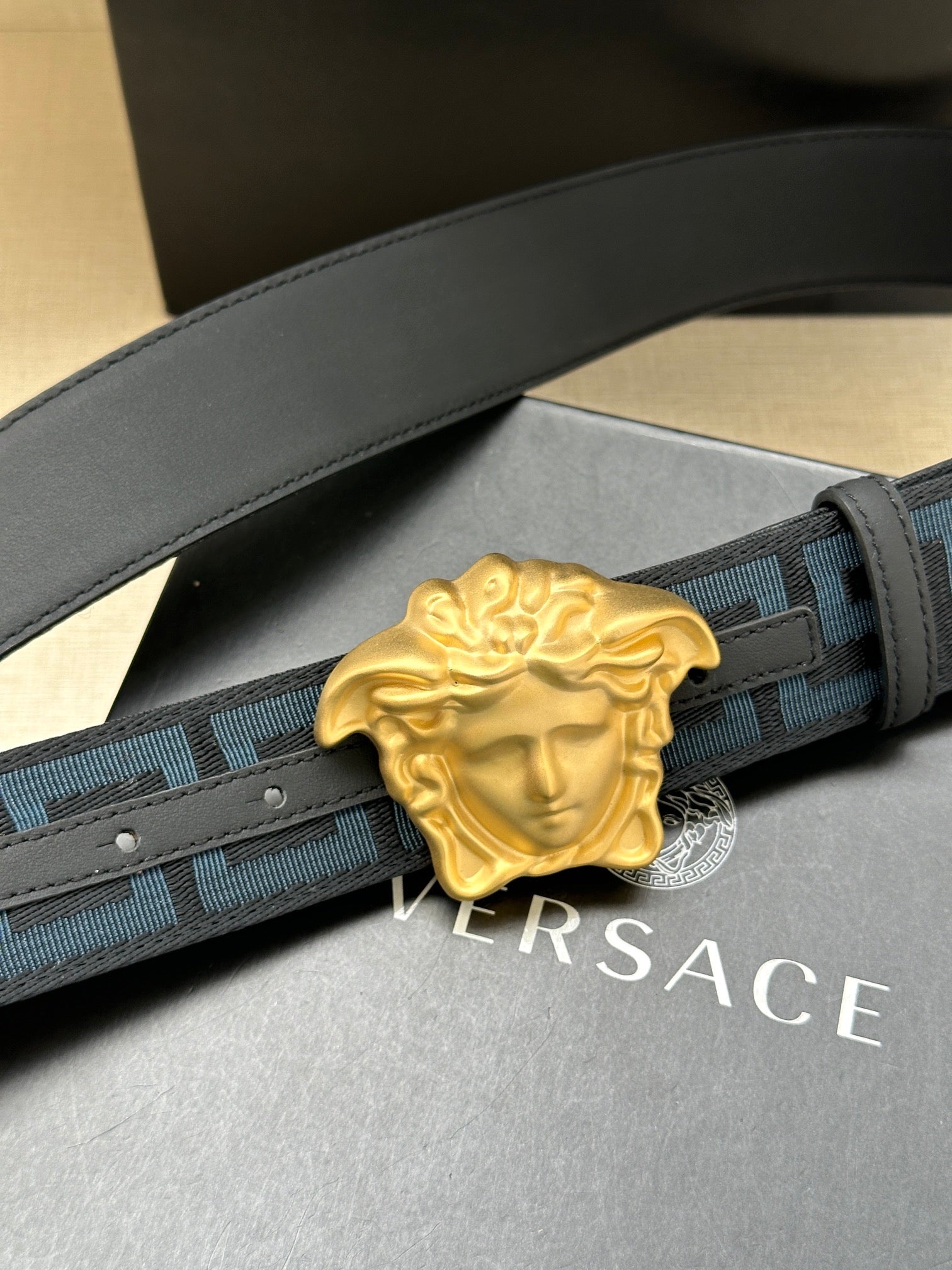 Versace belt close-up: blue Greca webbing and gold Medusa buckle on dark strap