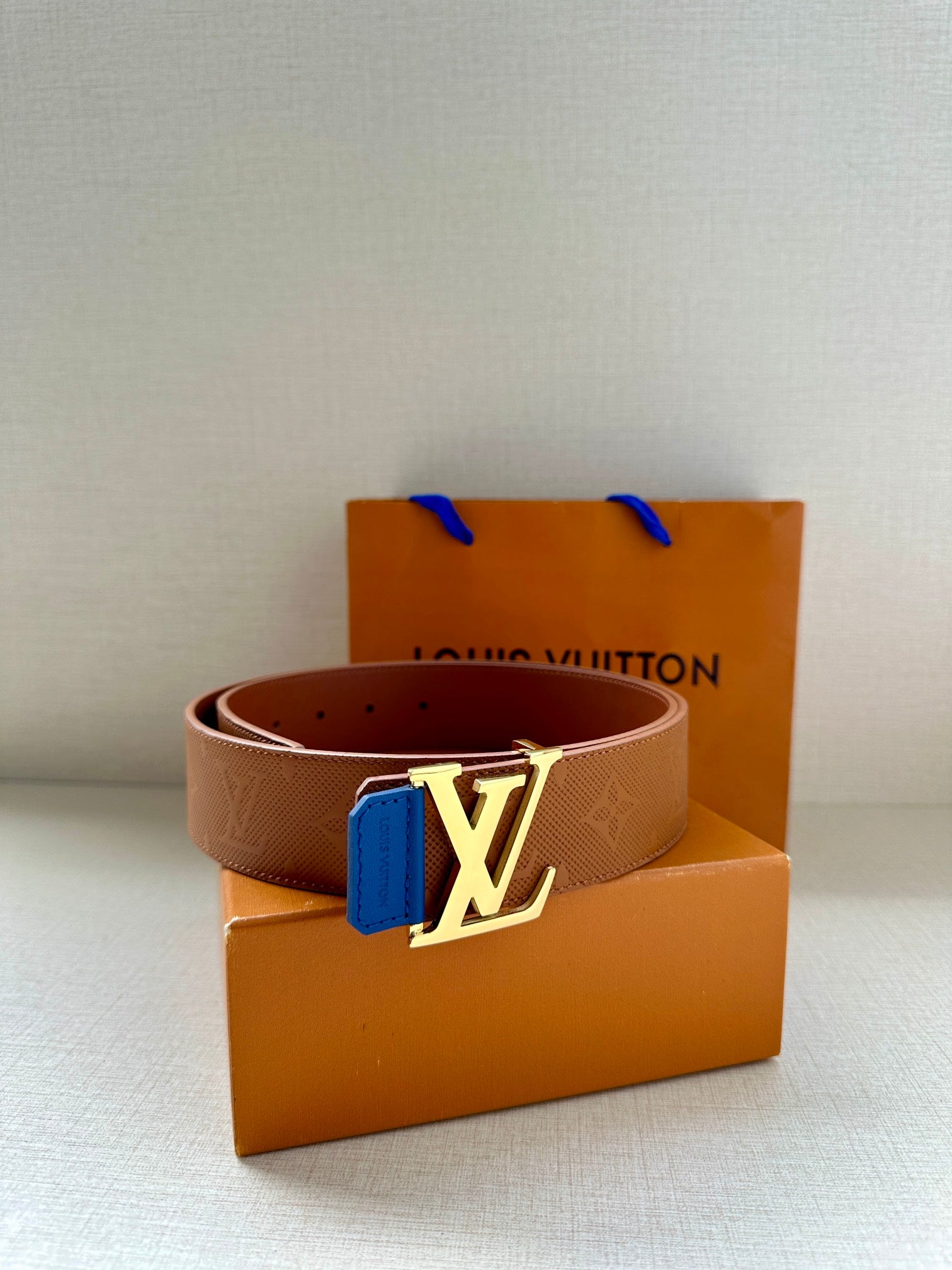 Tan monogram belt with silver LV buckle and blue keeper tab, front view