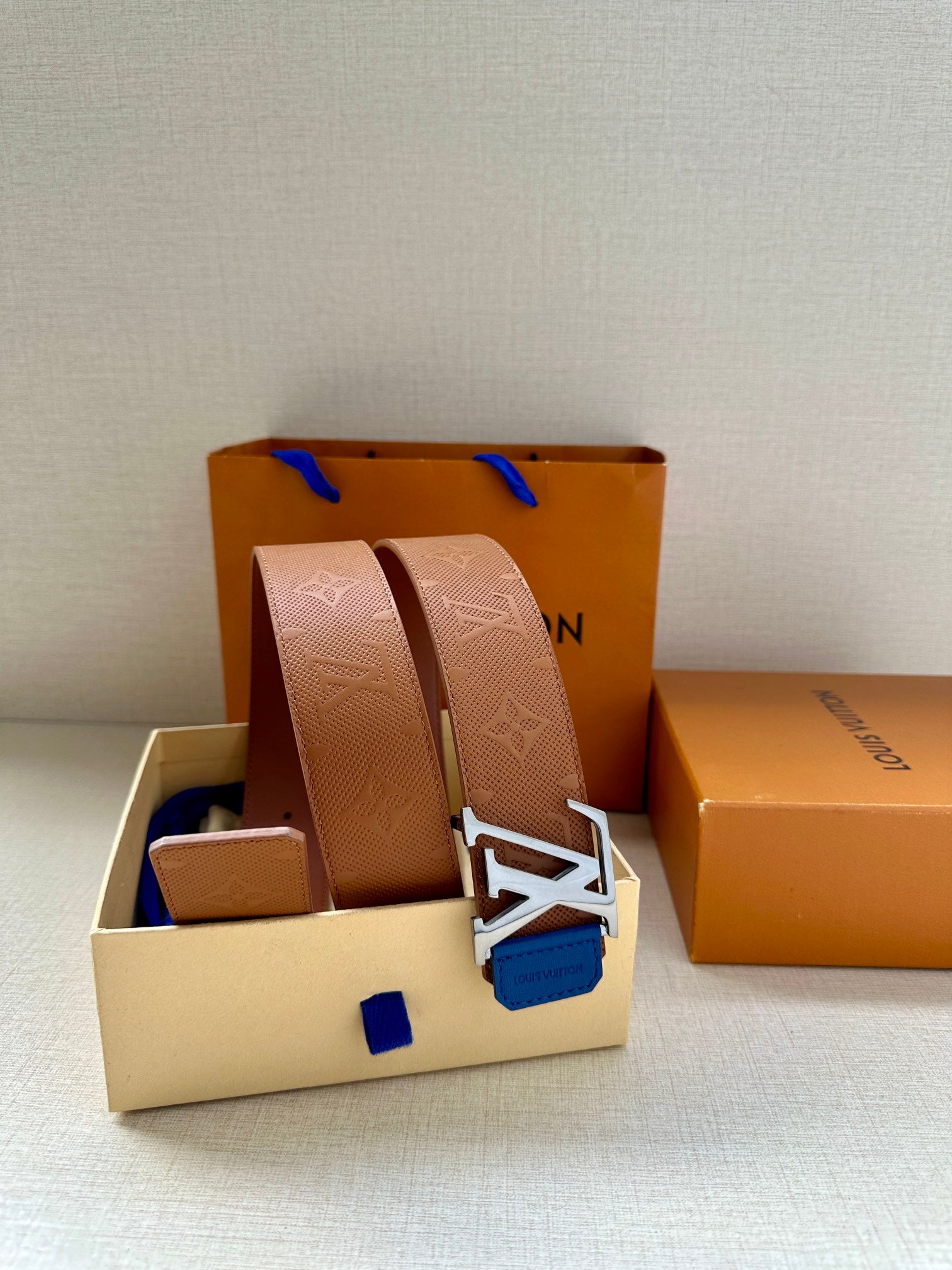 Tan monogram belt with silver LV buckle and blue keeper tab, close-up