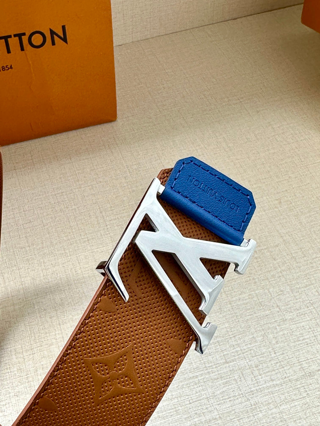 Tan monogram leather belt with silver LV buckle and blue keeper tab