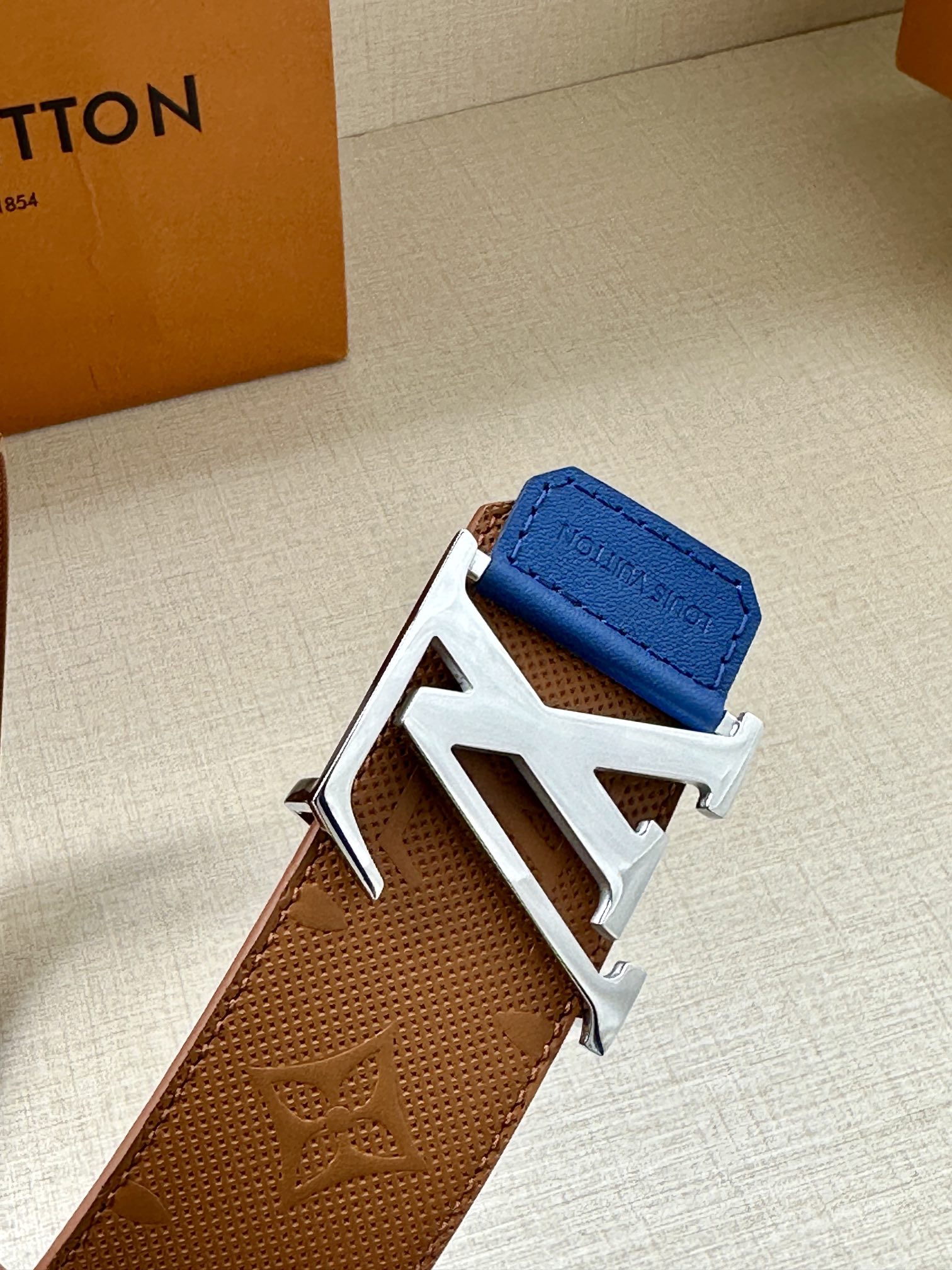 Tan monogram leather belt with silver LV buckle and blue keeper tab