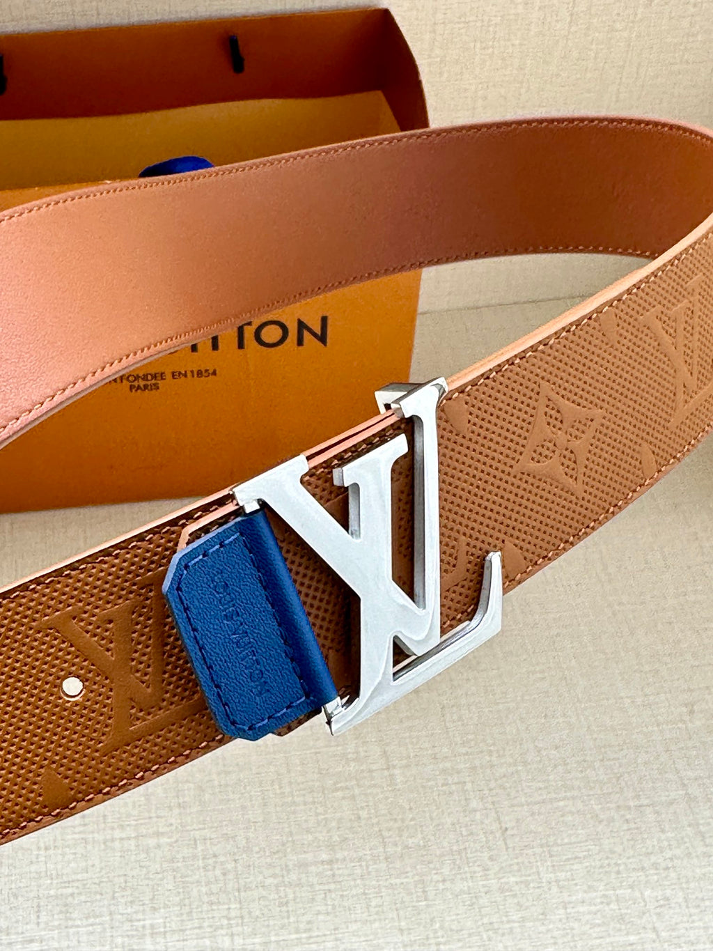 Tan monogram belt with large silver LV buckle and blue leather keeper