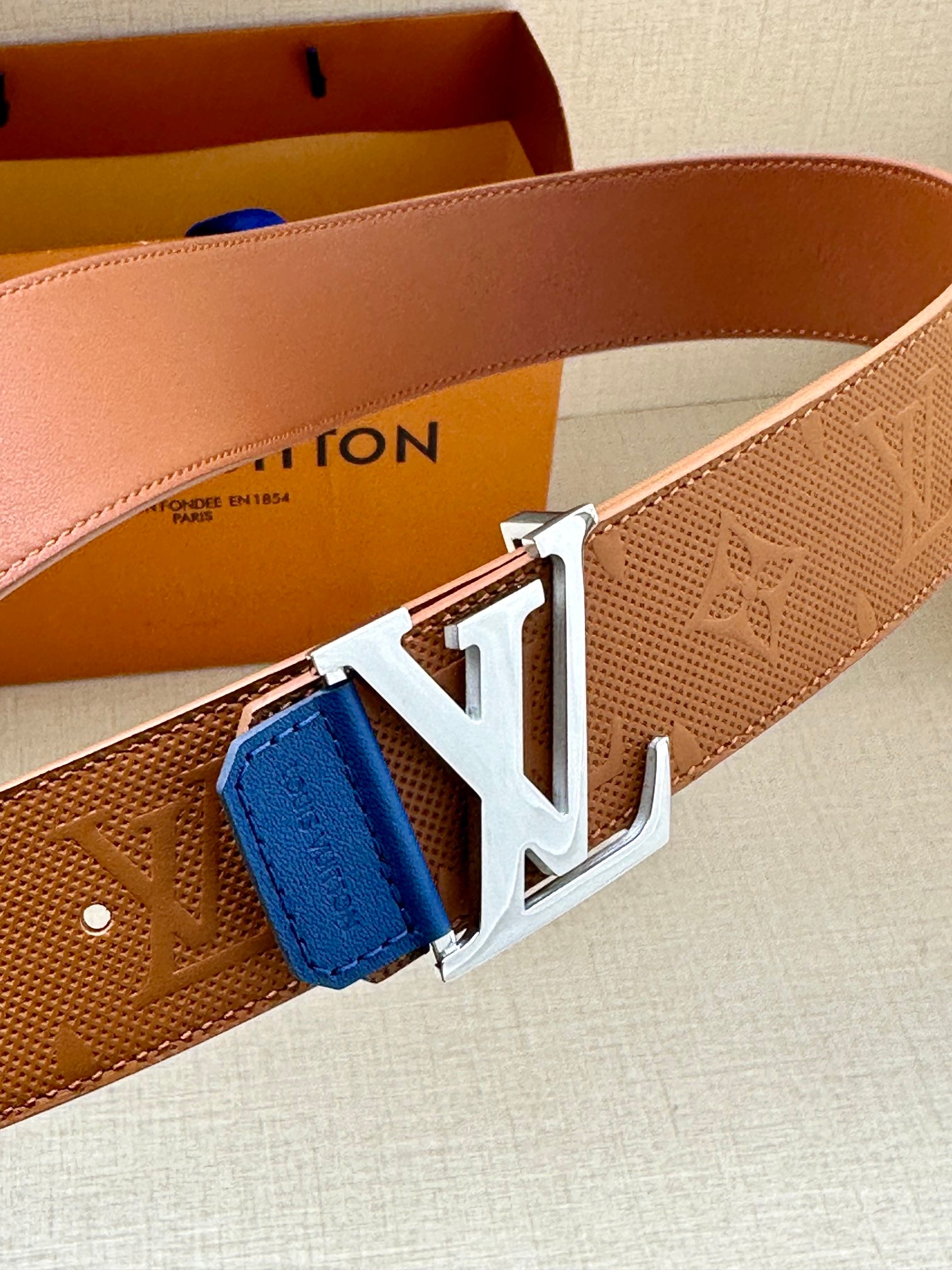 Tan monogram belt with large silver LV buckle and blue leather keeper