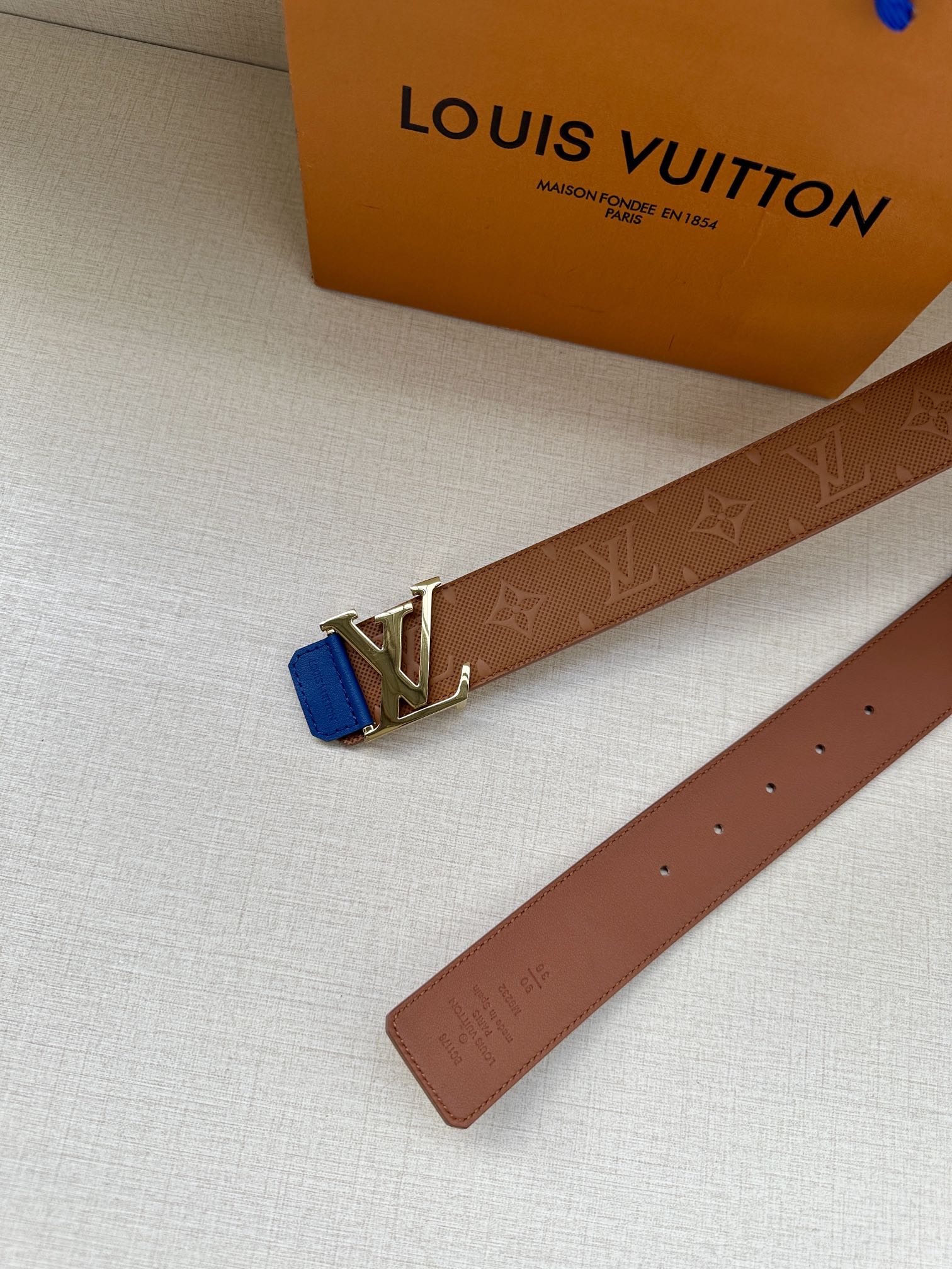 Tan leather belt end with silver LV buckle and blue keeper tab