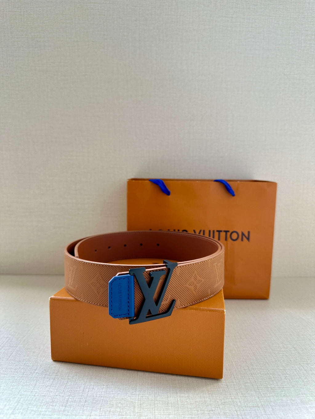Tan belt with blue LV buckle and embossed texture, with adjustable hole spacing visible