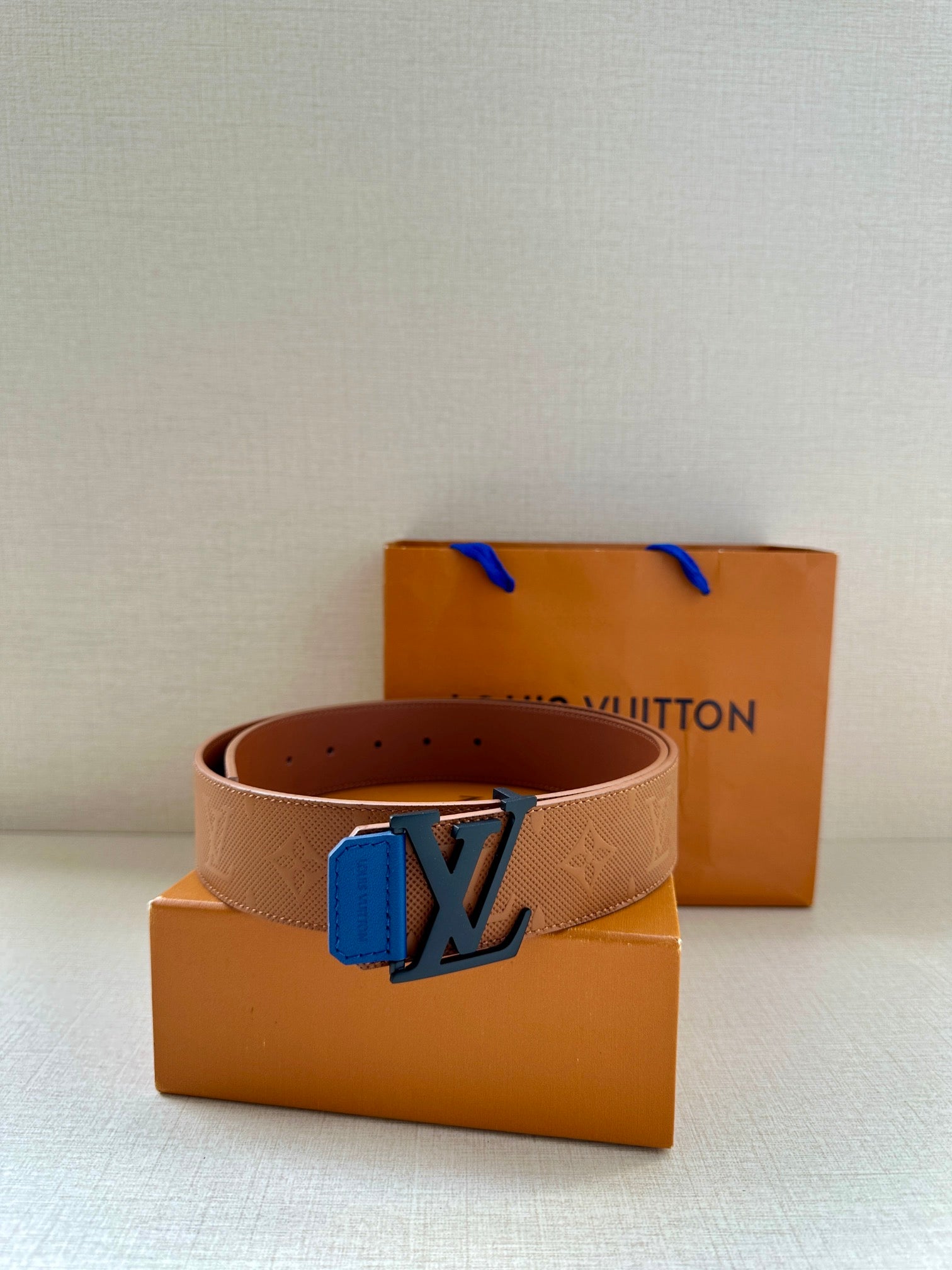 Tan belt with blue LV buckle and embossed texture, with adjustable hole spacing visible