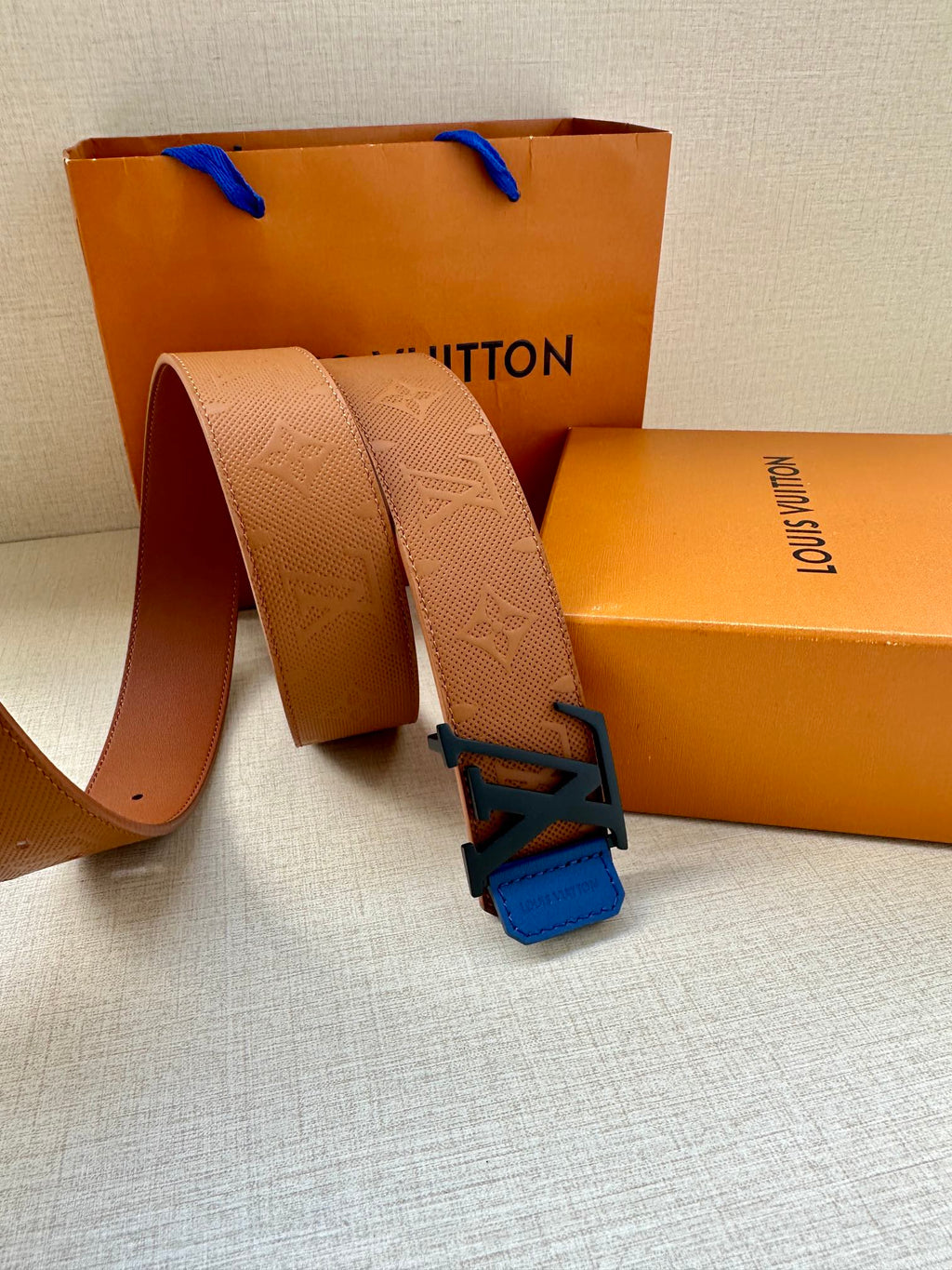 Tan belt strap looped with blue LV buckle and embossed monogram-style texture