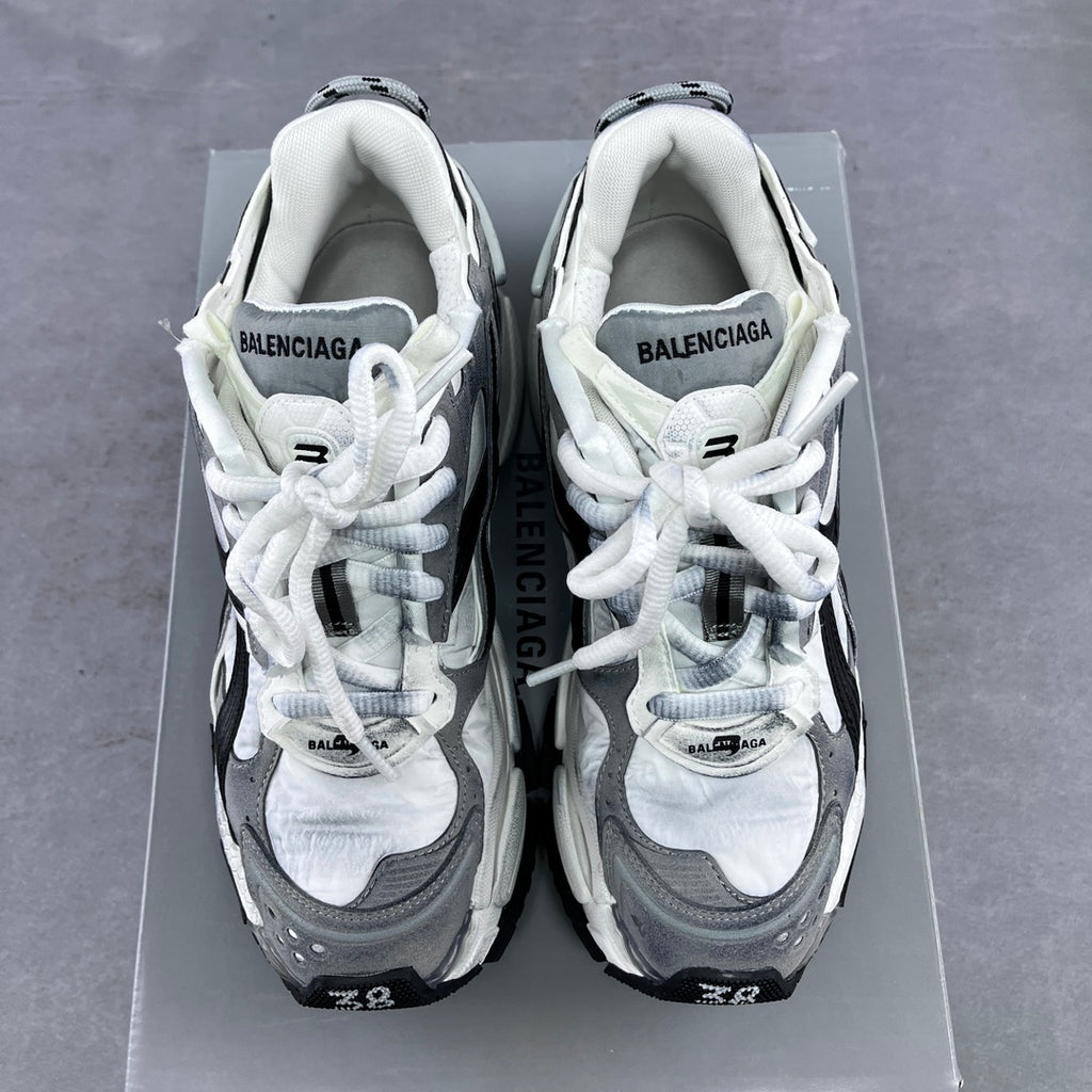 Athletic sneaker pair with white uppers, grey panels, and white laces on a box