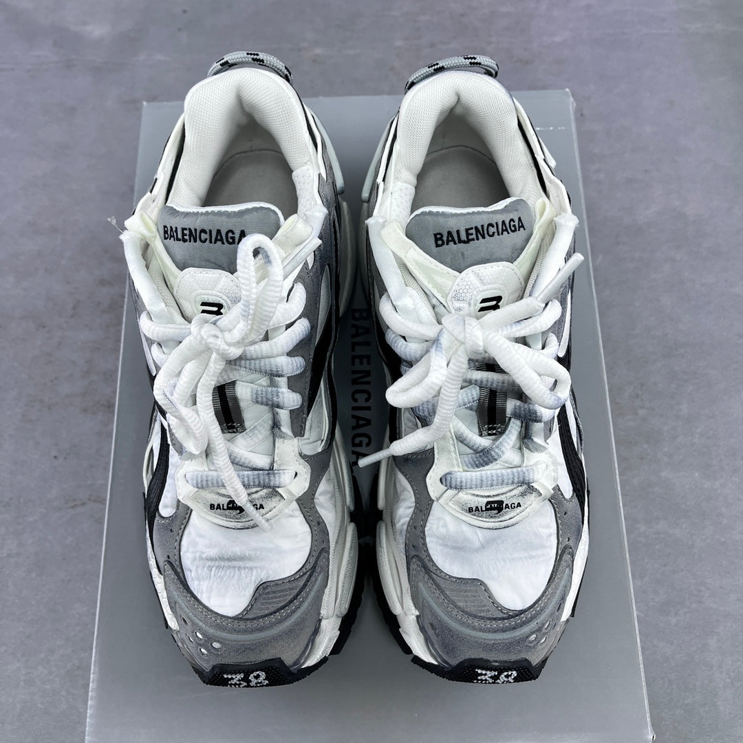 Athletic sneaker pair with white uppers, grey panels, and white laces on a box