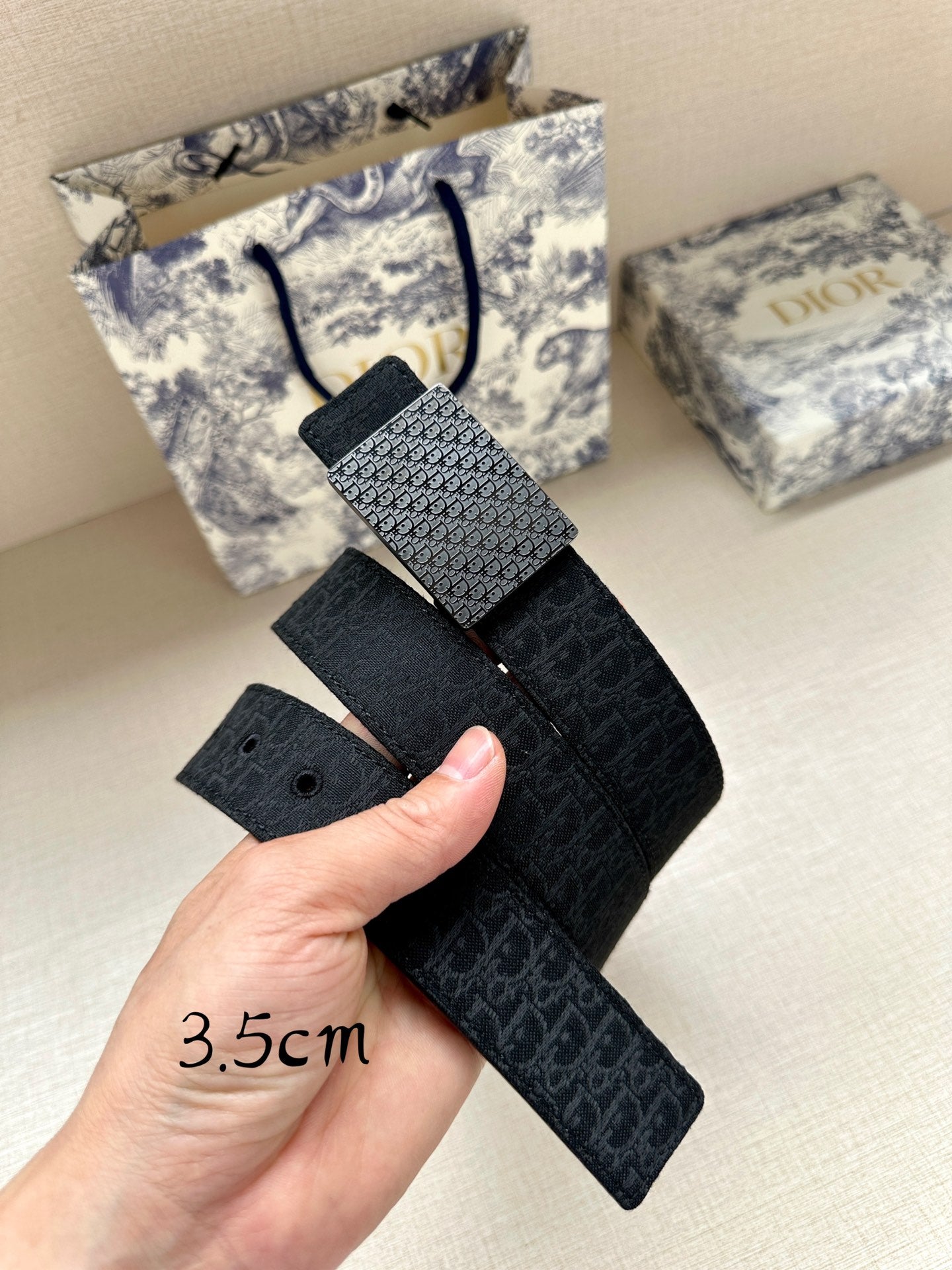 Dior belt with textured dark leather strap and square buckle, held in hand.