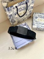 Dior belt with dark leather strap and textured monogram buckle, angled view.