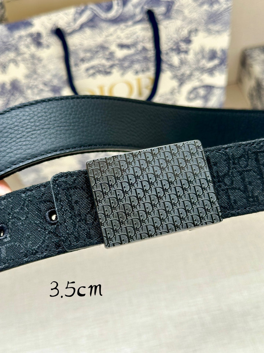 Dior belt close-up: dark leather strap with Dior monogram buckle panel.