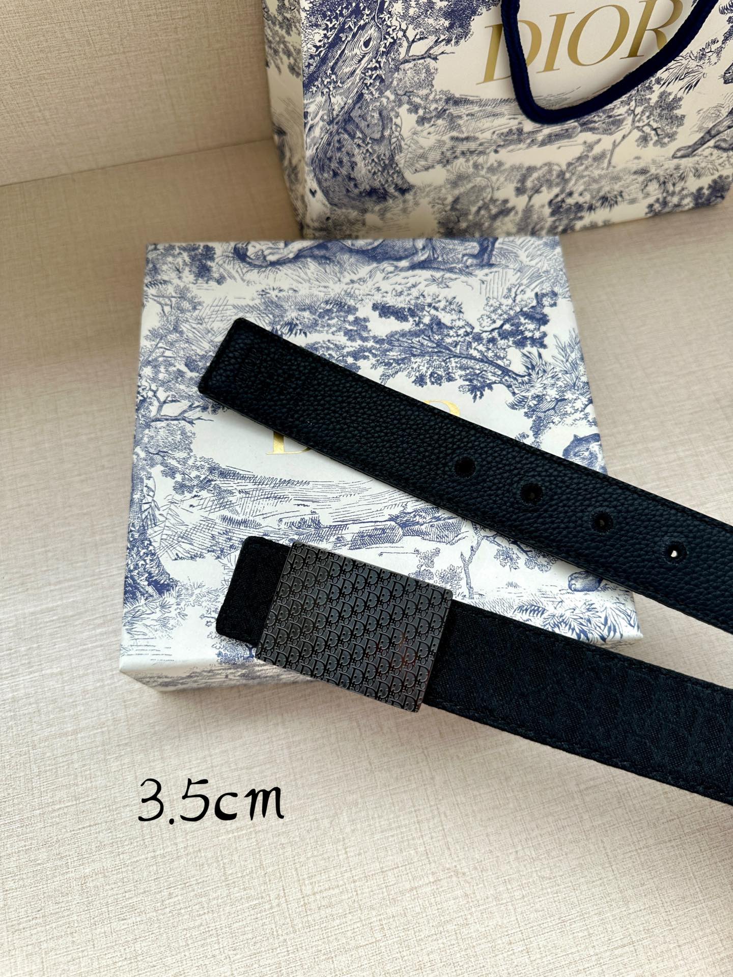 Dior belt with dark leather strap, eyelet holes, and textured monogram buckle panel.