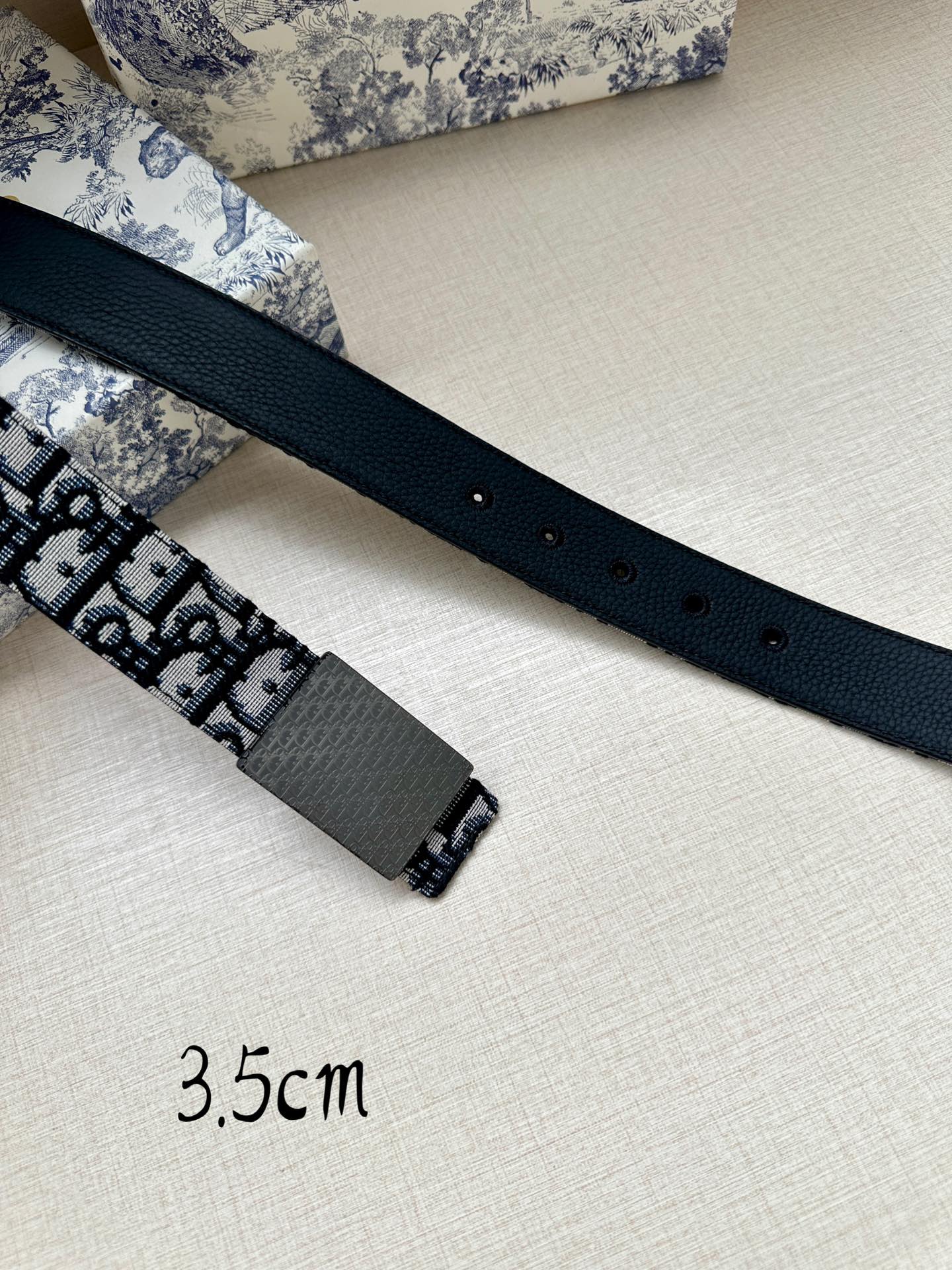 Dior belt flat lay with navy strap, logo panel, gray buckle and punched holes, 3.5cm