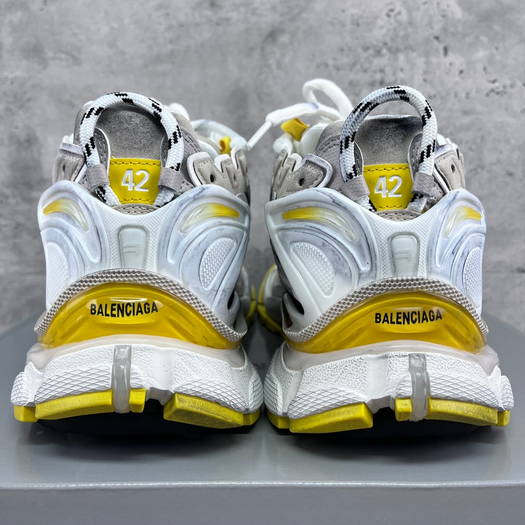 Pair of sneakers with Balenciaga heel logos and yellow heel trim on white uppers.