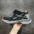 Side view of chunky black and gray sneakers with silver stripes and orange trim.