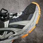 Quarter view of black and gray sneakers with textured silver panel and orange edge.