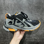 Chunky black and gray sneakers with orange laces and side stripes.
