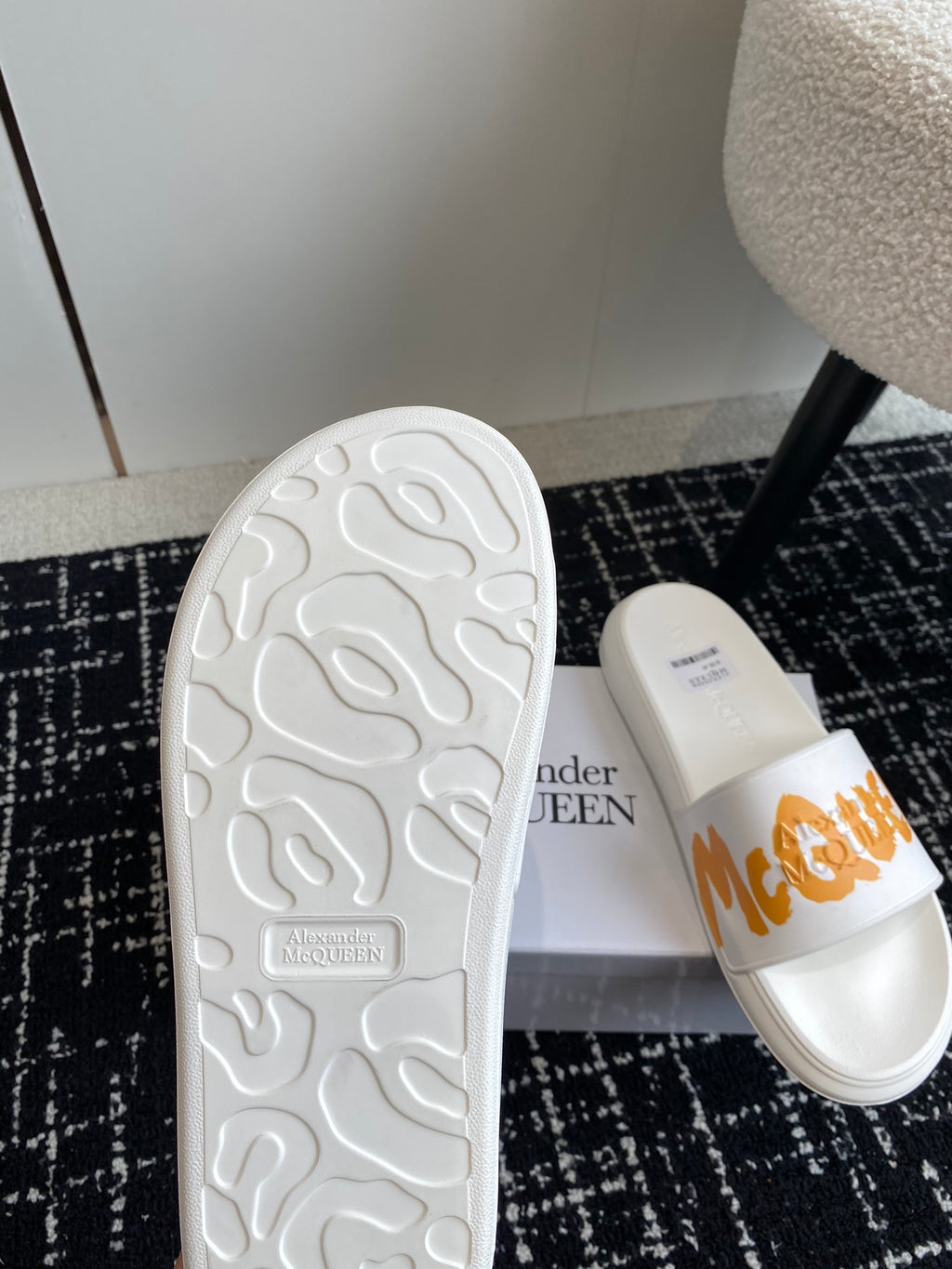 White slide sandals with textured outsole and orange logo strap on upper.
