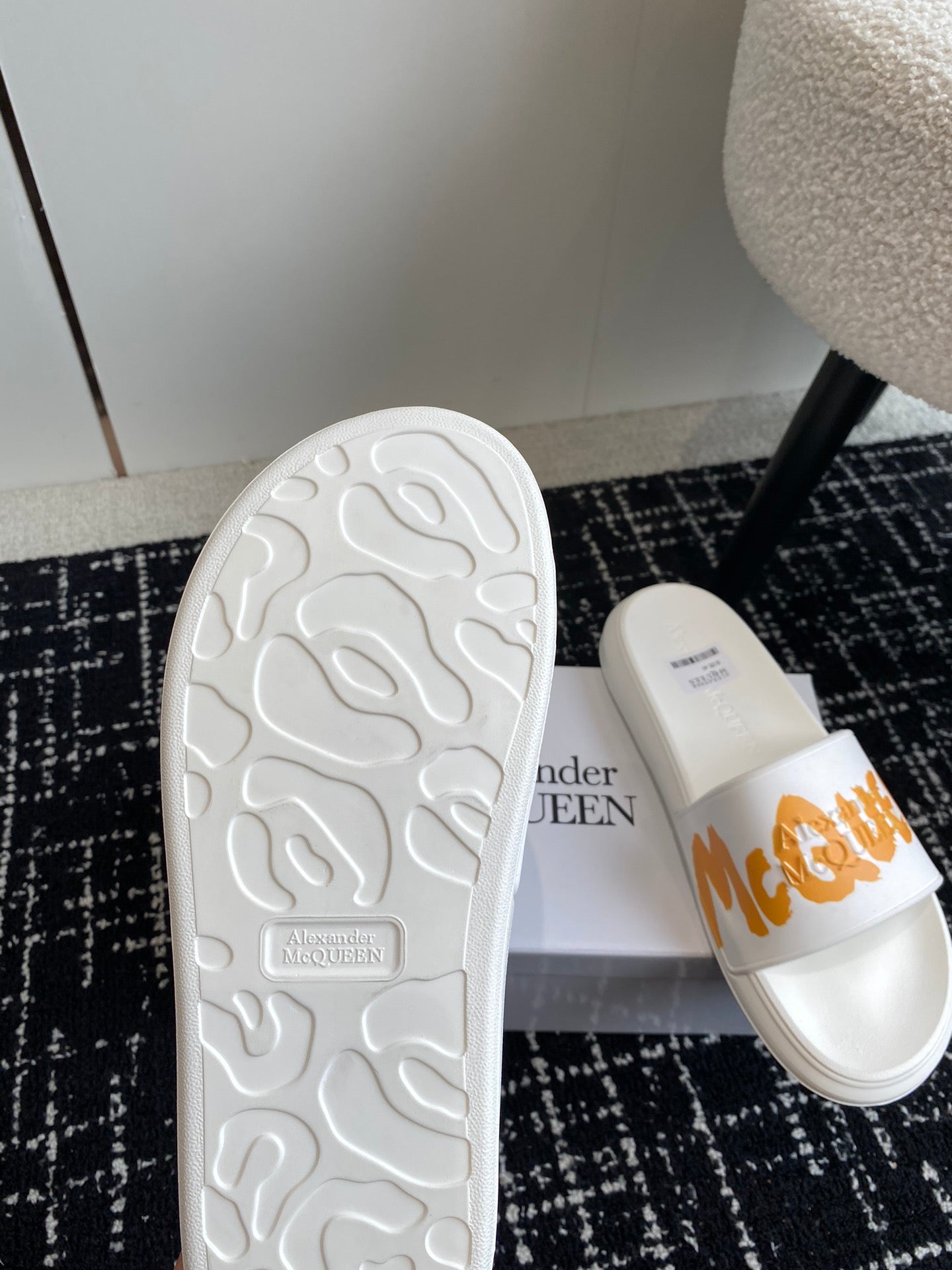 White slide sandals with textured outsole and orange logo strap on upper.