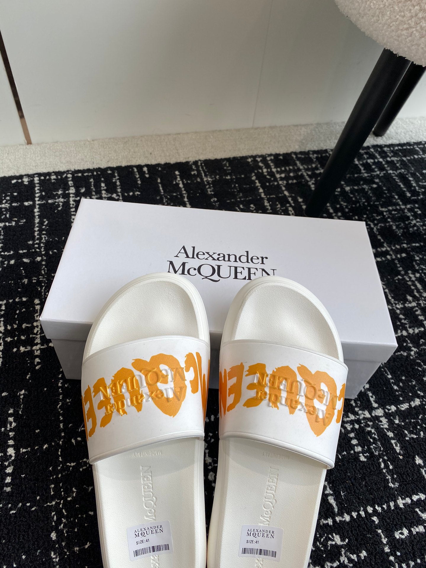White slide sandals with orange logo strap and smooth cushioned footbeds.