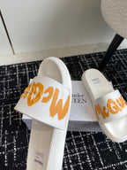 White slide sandals with orange logo strap, side view with thick sole.