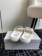 White slide sandals with orange logo strap, showing heel area and back view.