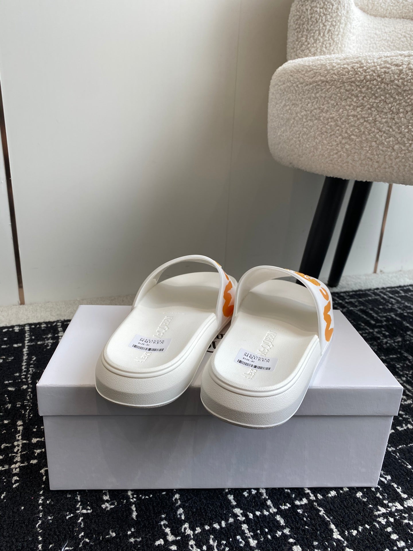 White slide sandals with orange logo strap, showing heel area and back view.