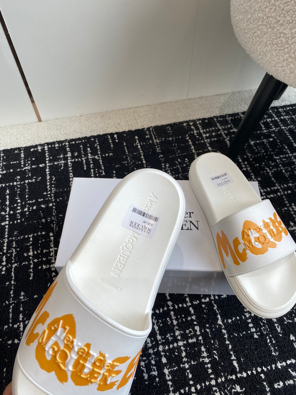 White slide sandals with orange logo strap, two shoes angled on a box.