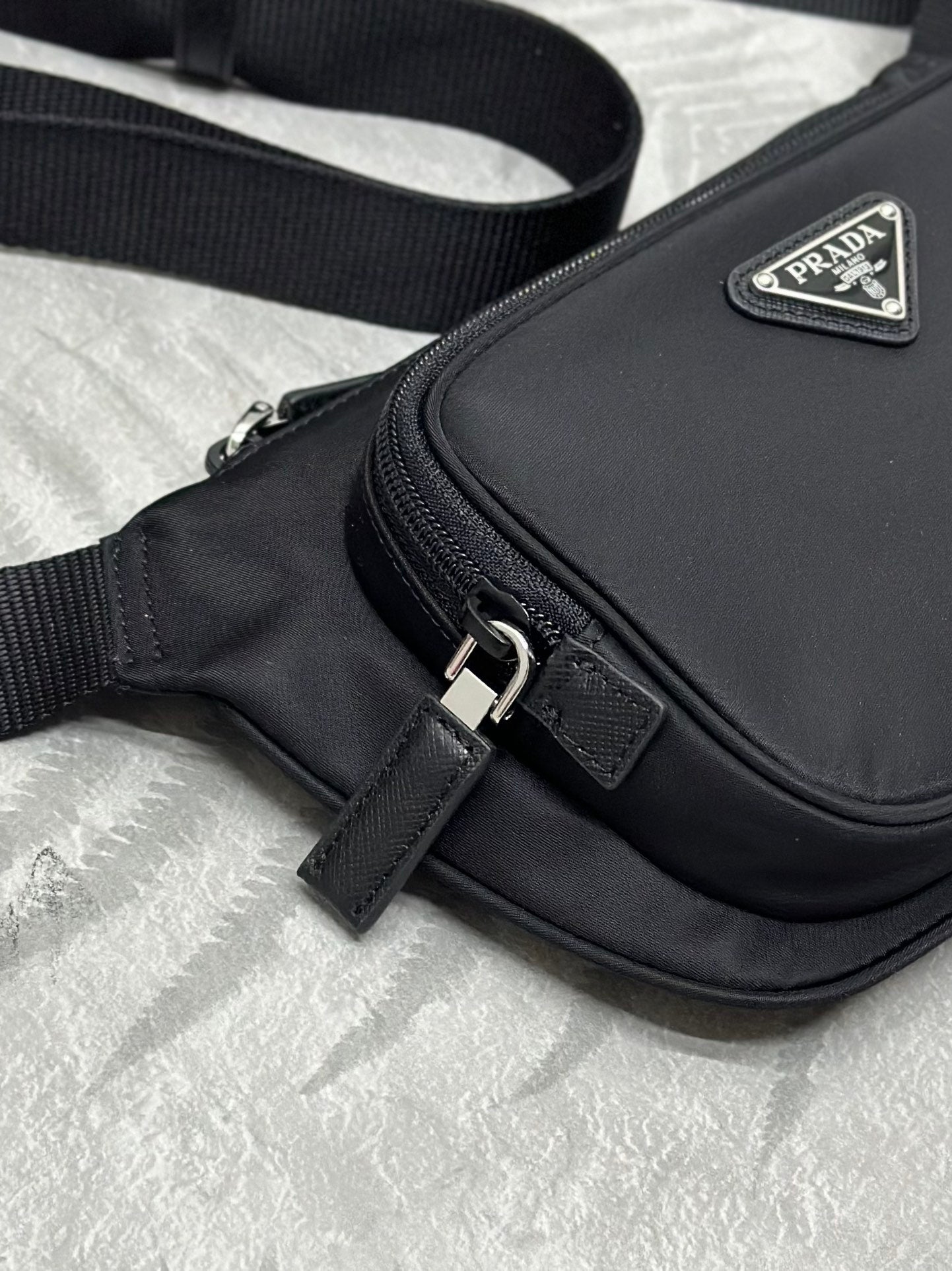 Black crossbody bag front with metal buckle and triangular PRADA logo plaque