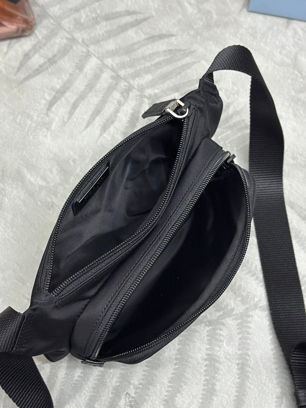 Black crossbody bag shown from side with dual zippers and front pocket